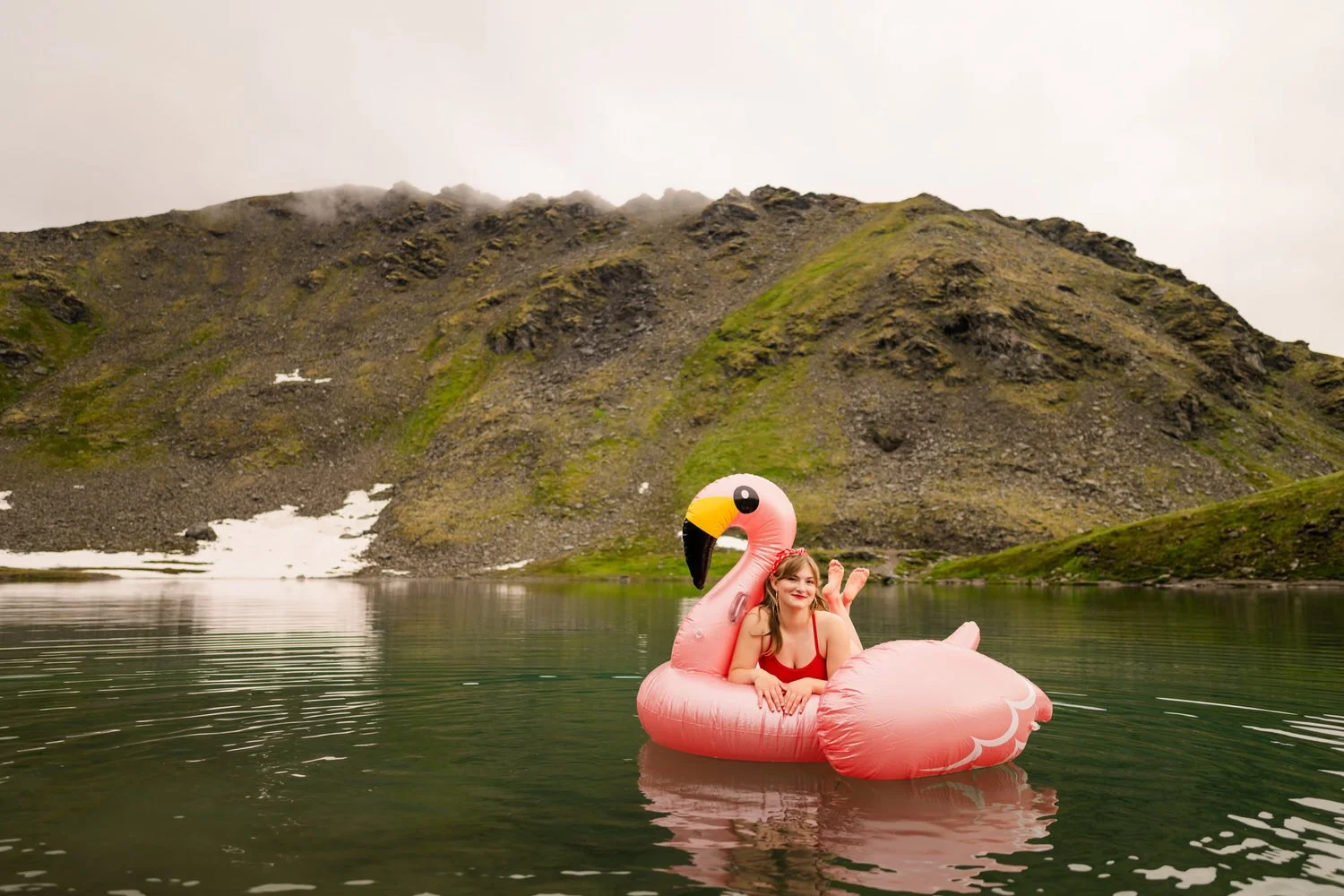 Girl floats on a flamingo floaty in an alaska lake in a red vintage swimming suit