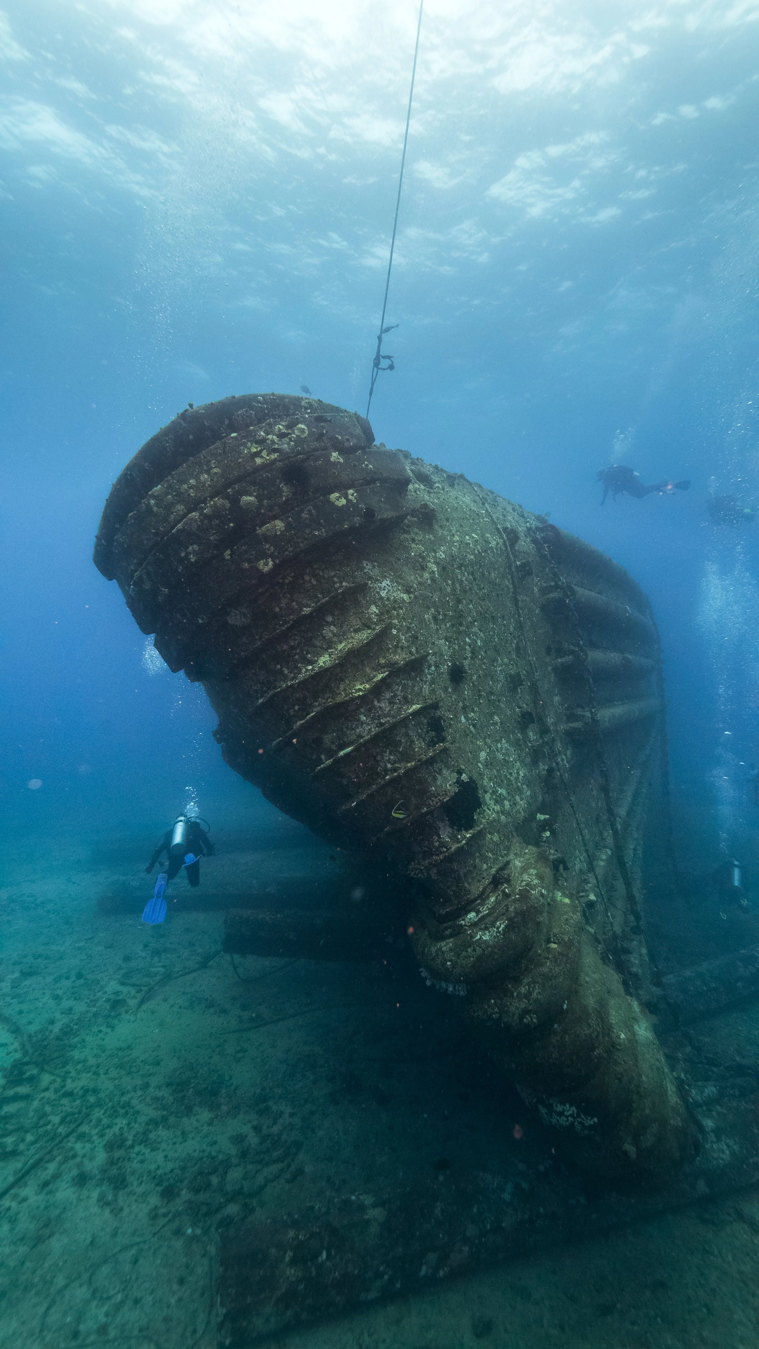 Underwater view of a sunken shipwreck with scuba divers exploring around it.
