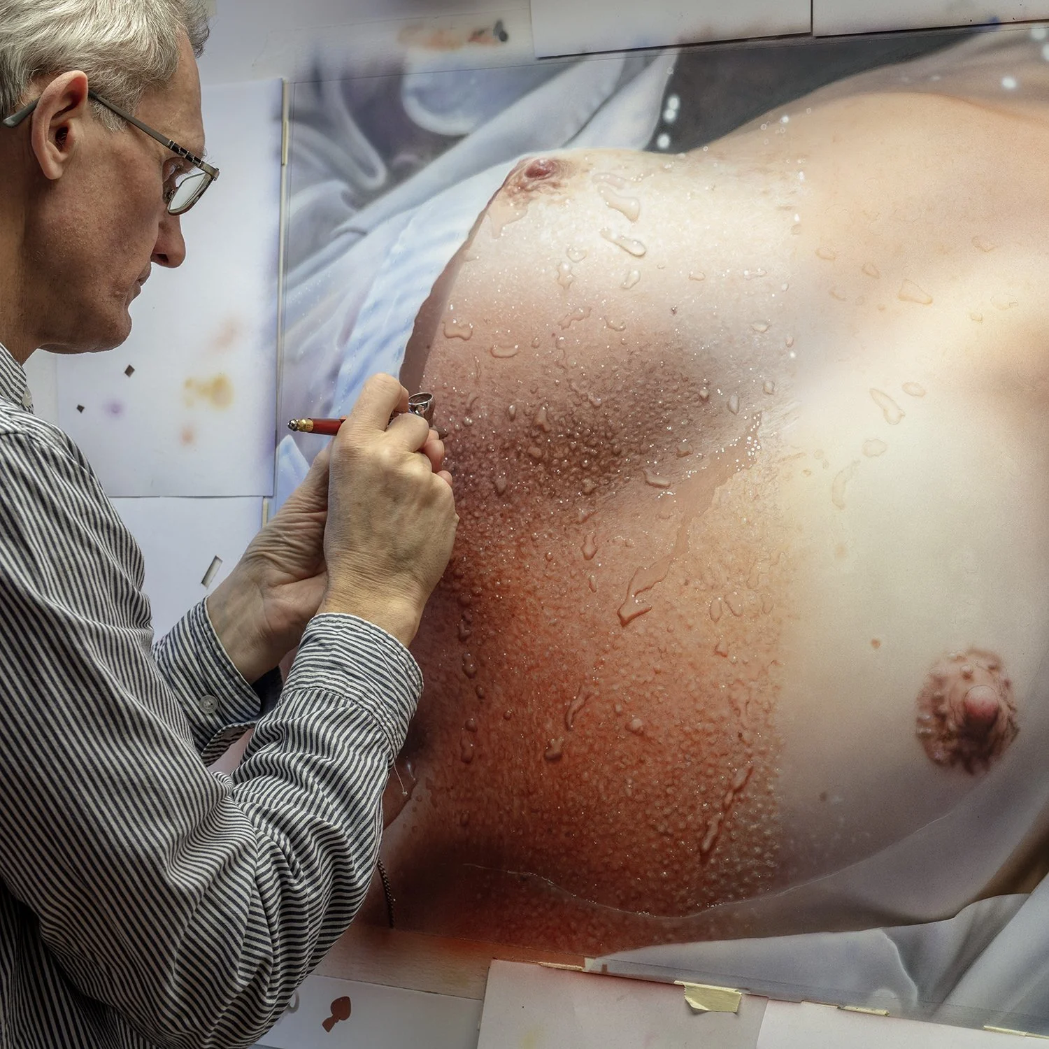 A man in glasses is sketching on a large image of a close-up of a strawberry. The photo is taken indoors, and the man is focused on his work.