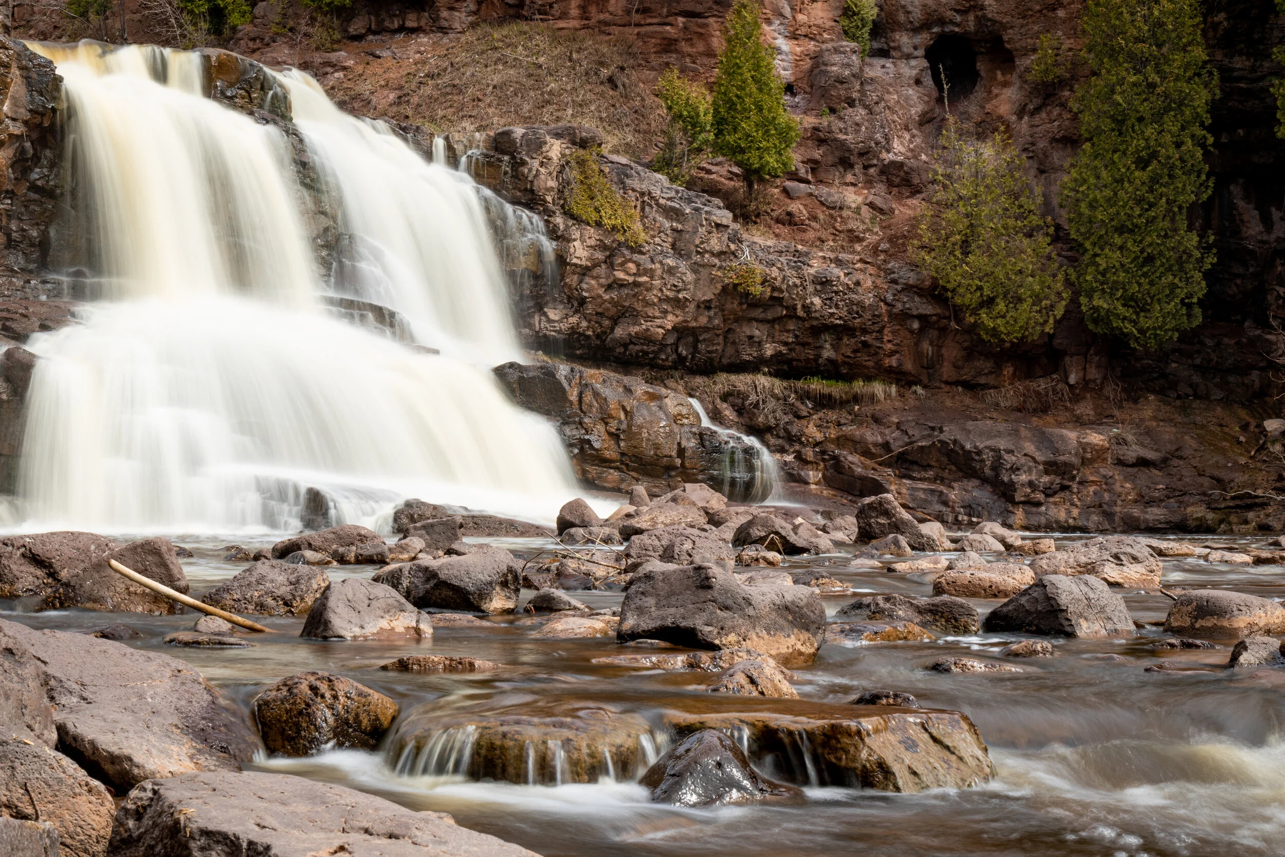 A waterfall cascading over rocks into a stream, surrounded by trees and rocky terrain.