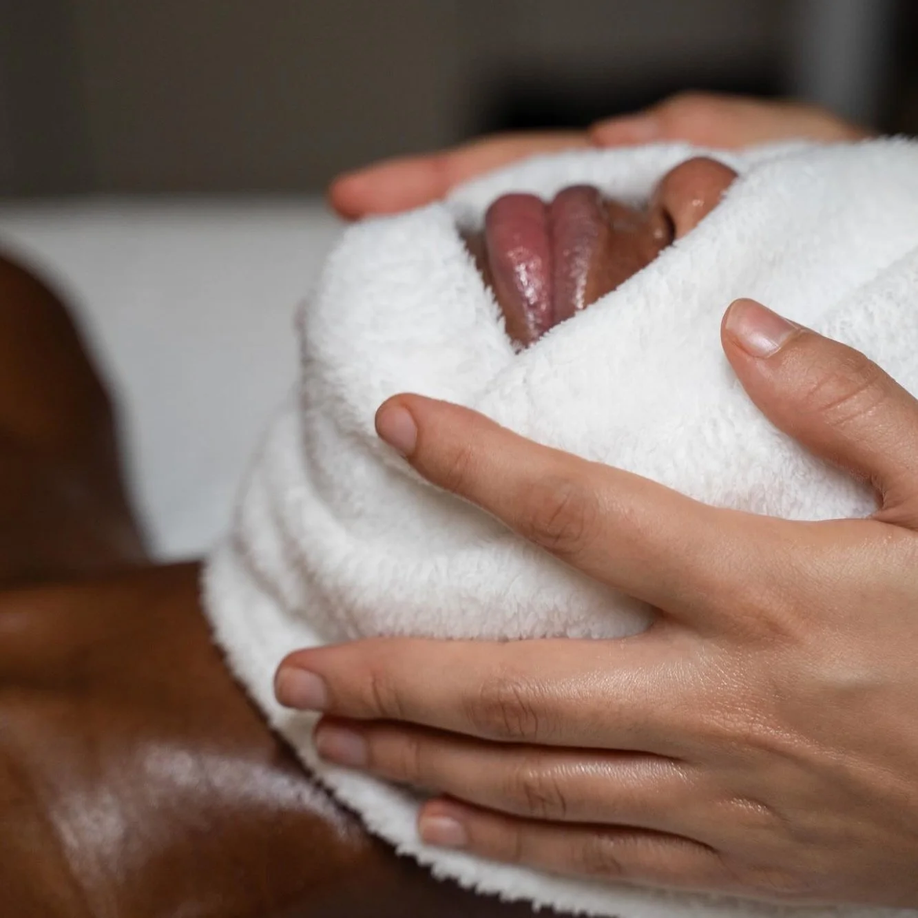 Person lying down covered with a white towel or blanket, with a woman’s hands gently holding the towel close to their face.