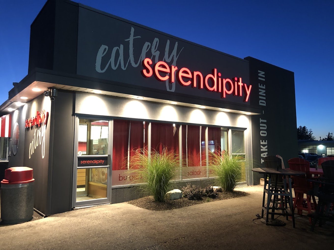 Exterior view of a restaurant called 'Serendipity' at dusk, with illuminated signage, red curtains inside the windows, outdoor seating - Signupsigns - Neustadt.