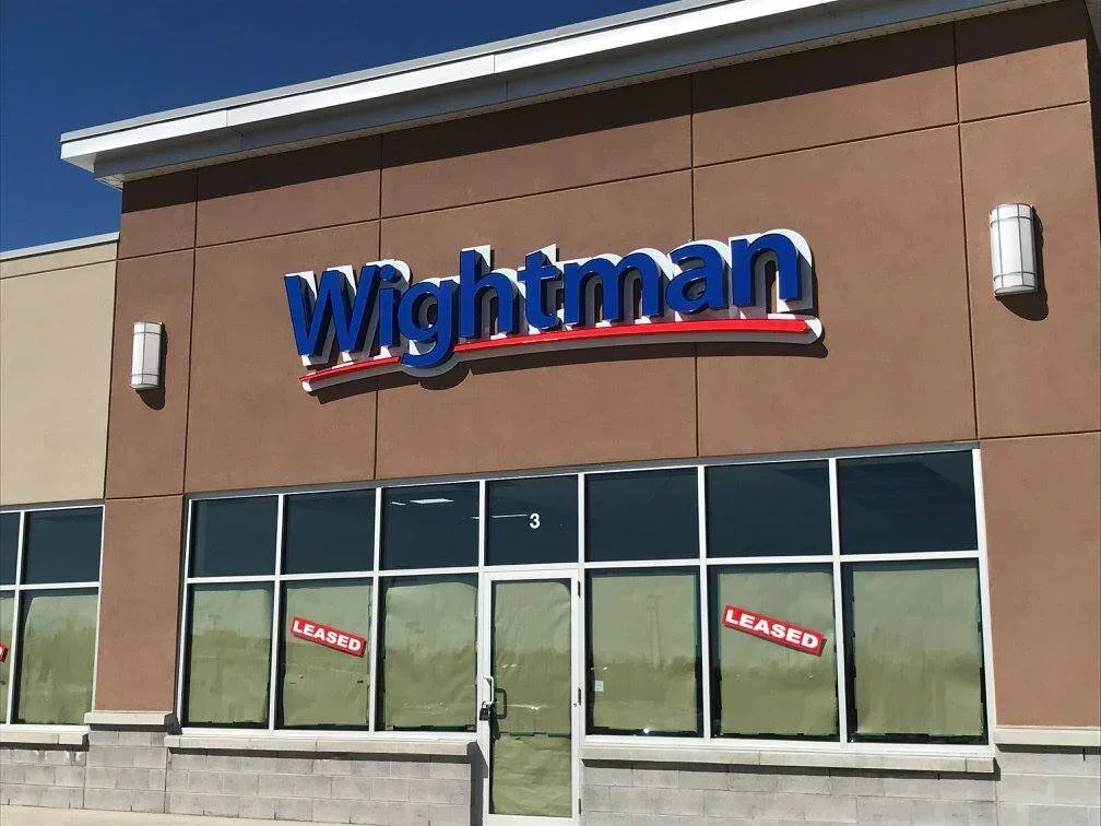 The front of a Wightman store with a sign on the building, large glass windows - Signupsigns - Neustadt.