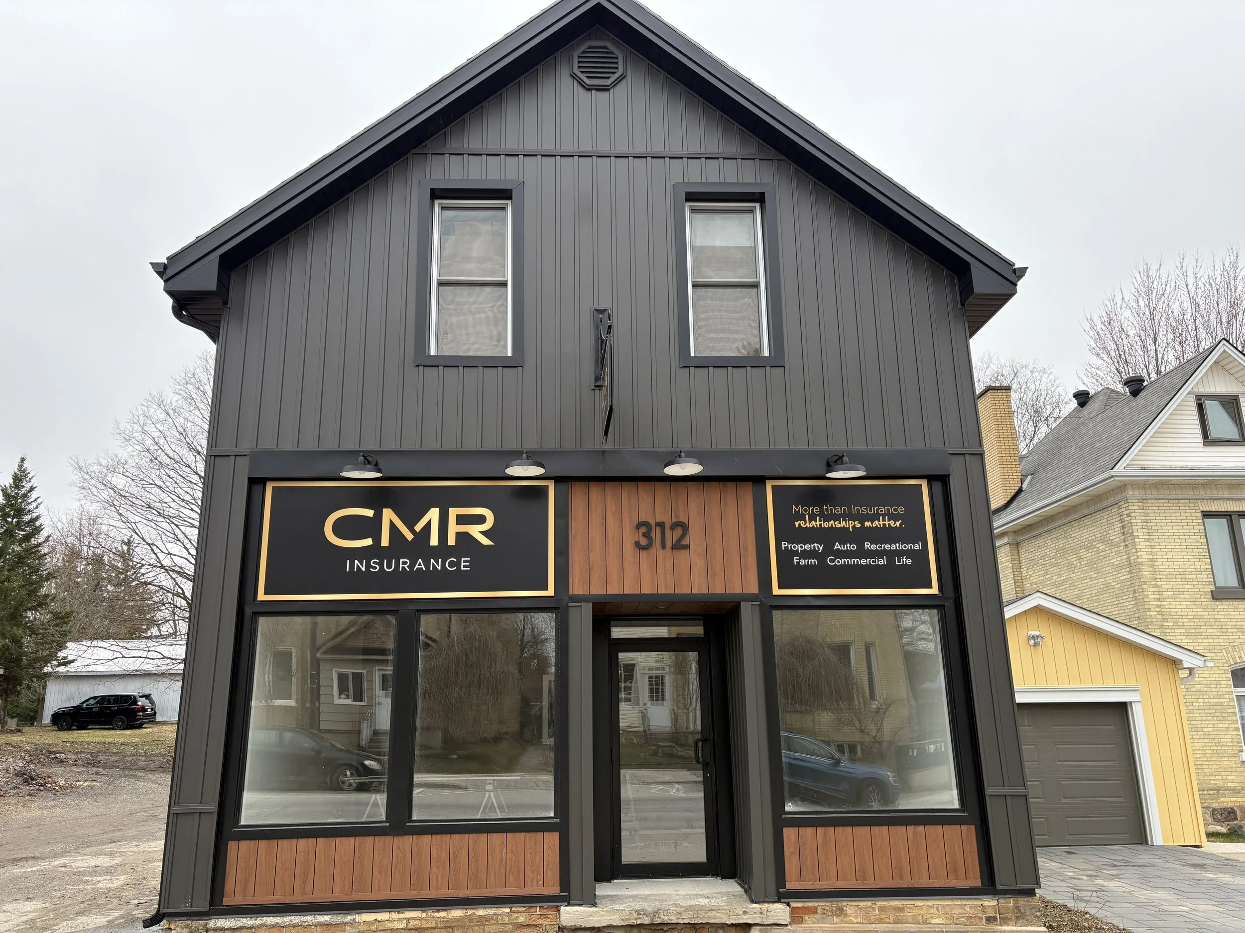 Storefront with a black sign that reads "CMR INSURANCE" in gold lettering, located at 312, with large glass windows and wooden paneling below the sign - Signupsigns - Neustadt.