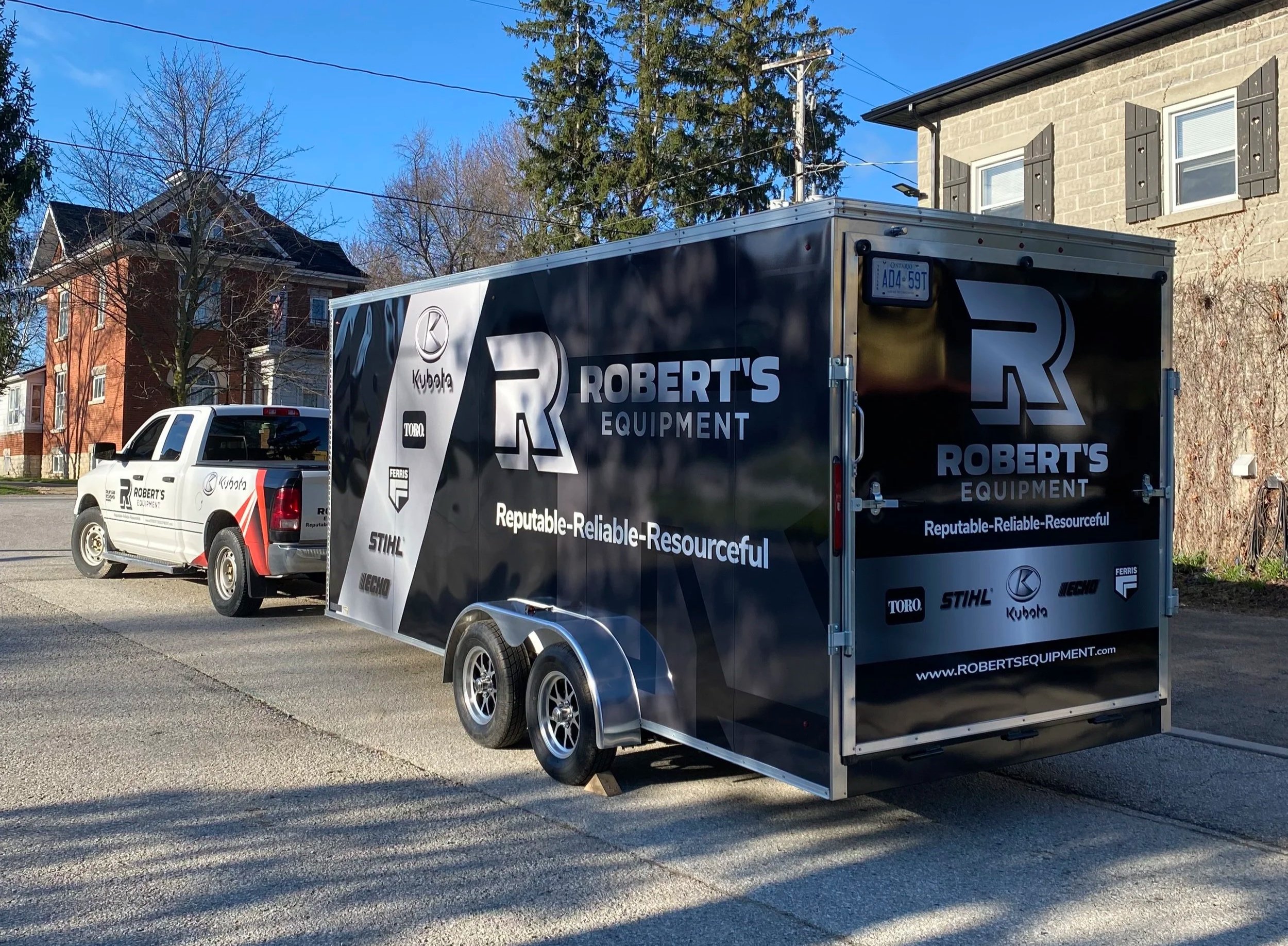 A pickup truck and a black enclosed trailer with the branding 'Robert's Equipment' parked on a residential street with houses and trees in the background. The trailer features logos of brands like Kubota, Toro, and Stihl - Signupsigns - Neustadt.