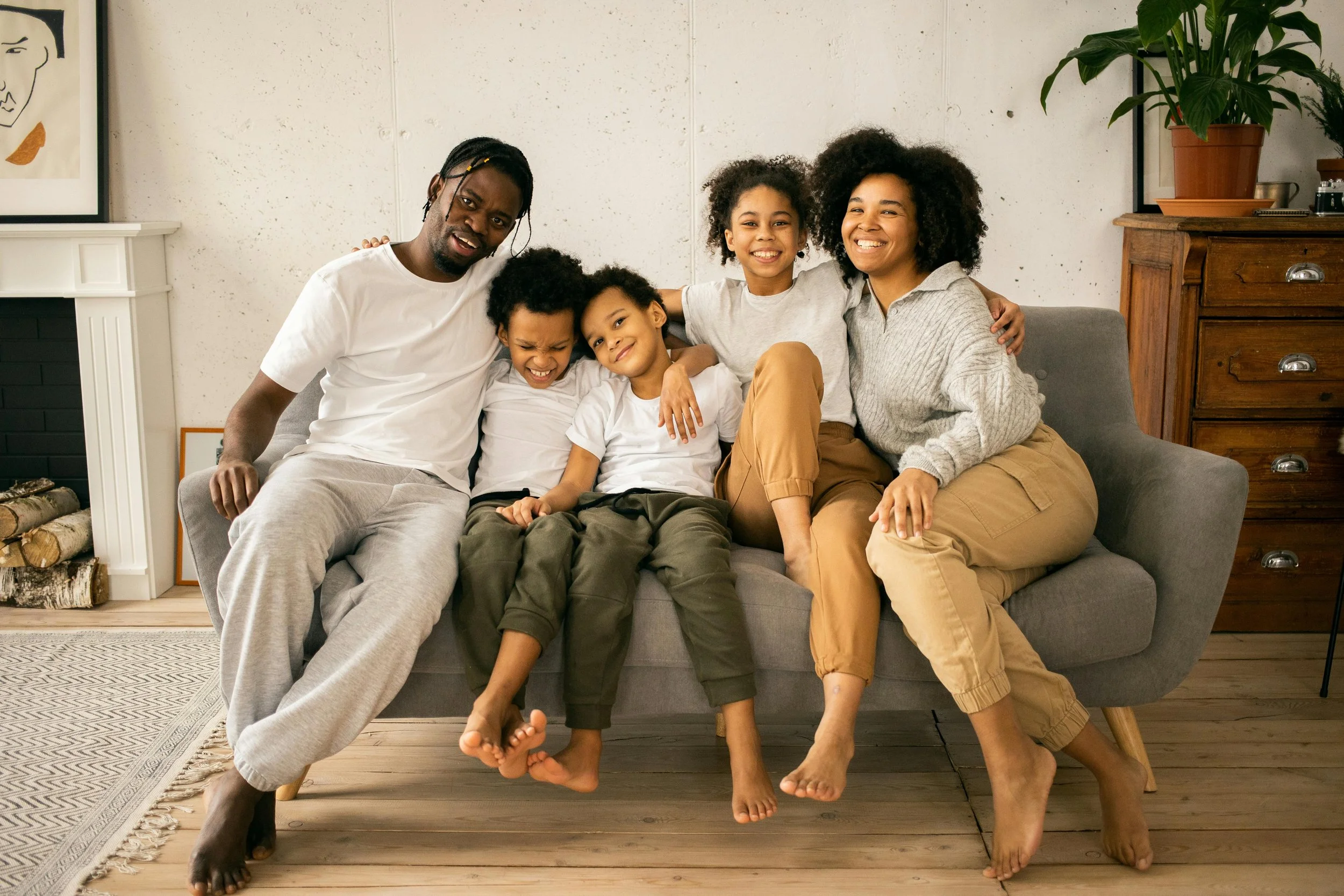 Family sitting on a gray couch in a cozy living room, smiling and laughing together.