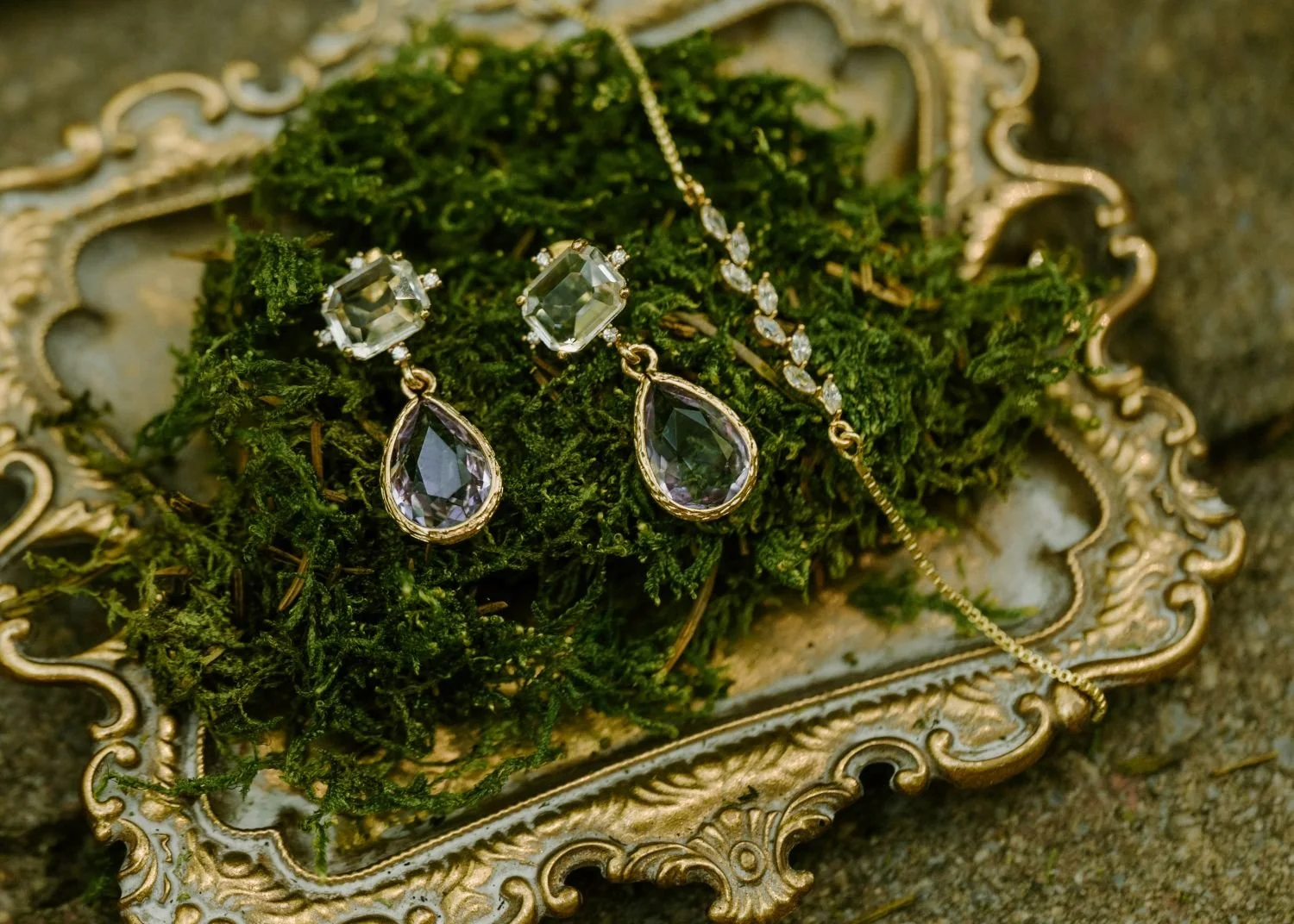 A detailed close-up of bridal earrings displayed on a moss covered gilded gold plate. Historic Jasmine a dreamy fairytale wedding venue in New Kent, Virginia.