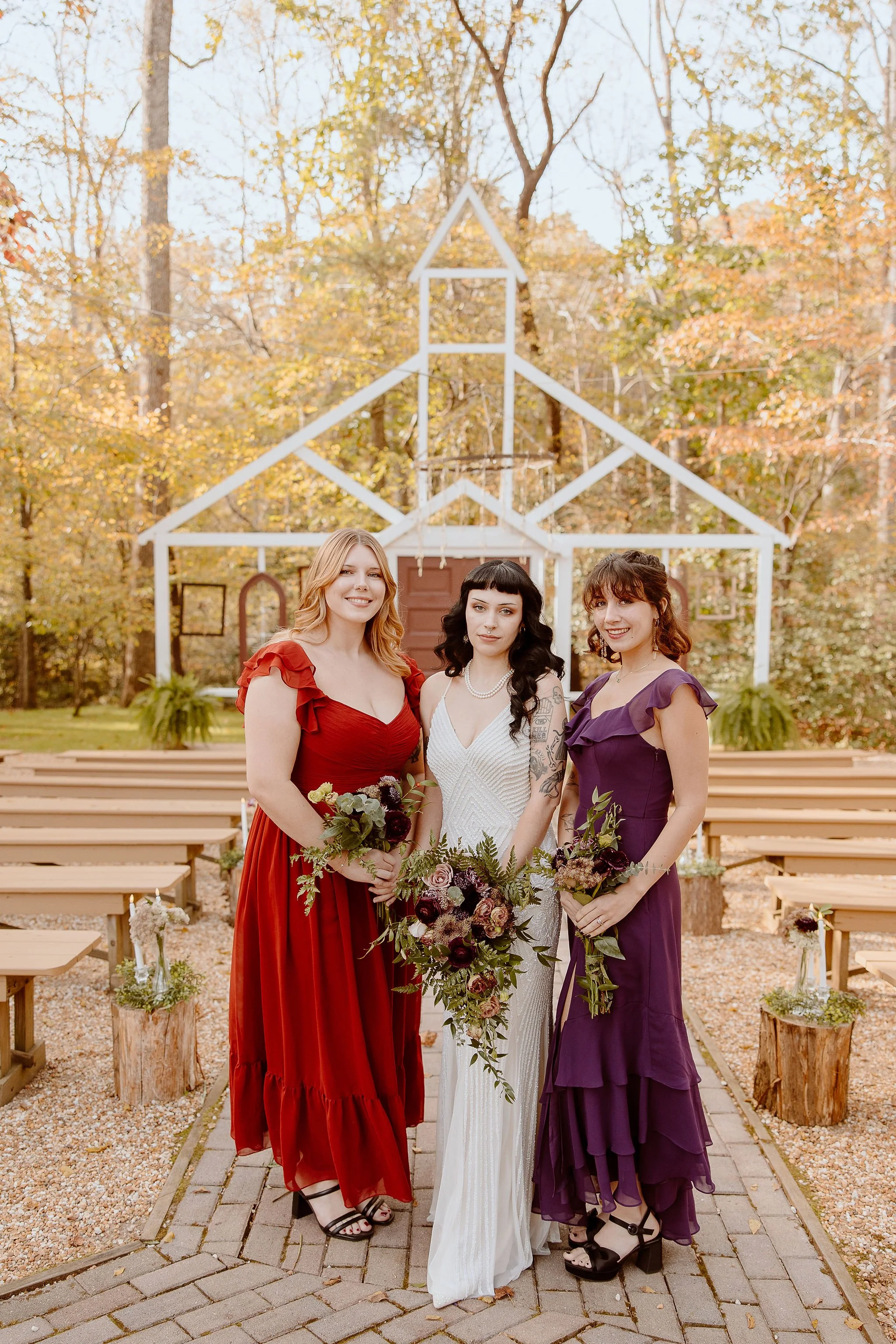 A bride and her bridesmaids posing in front of the Chapel in the Woods ceremony site at Historic Jasmine, a private wedding venue in New Kent, VA.