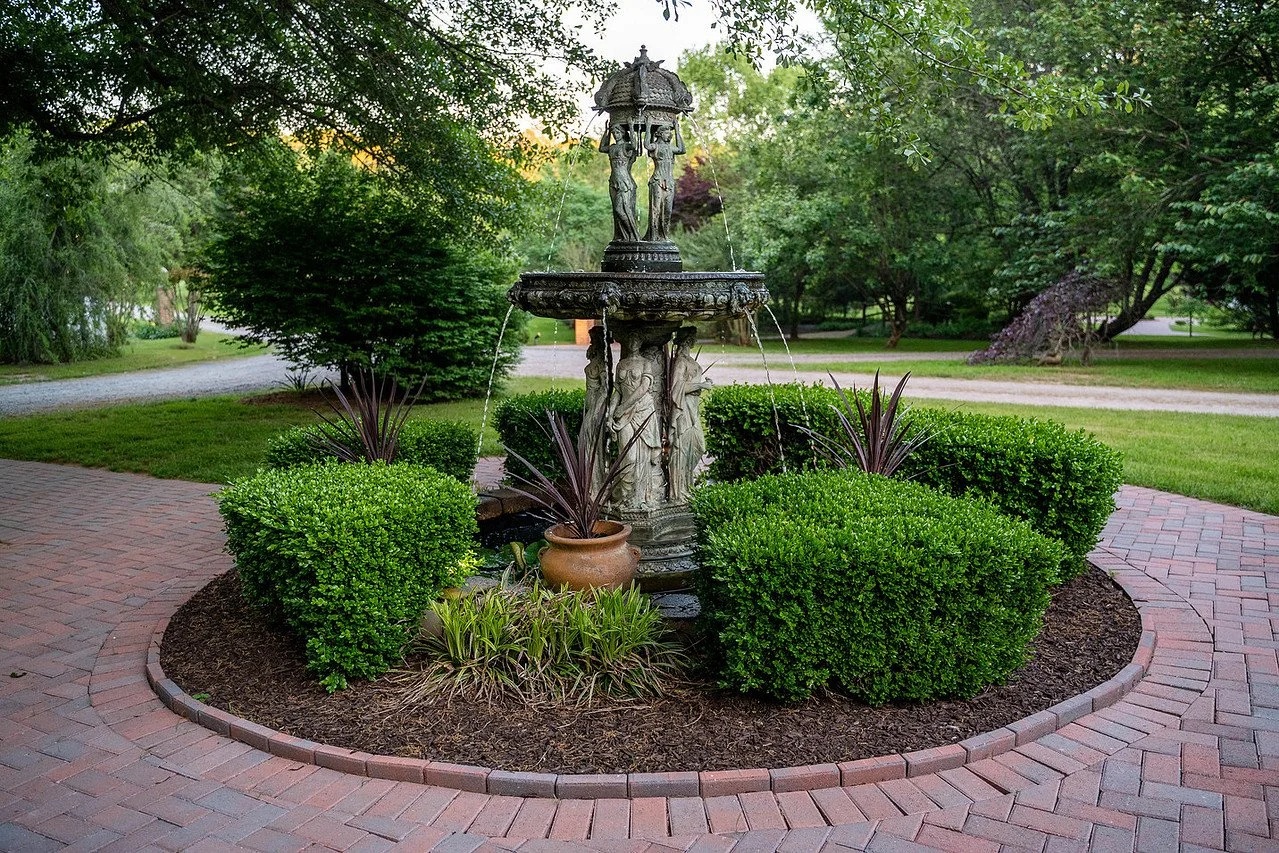 View of the bronze tiered fountain with circular brick pathway at the entrance of the Manor House | Historic Jasmine, a private wedding venue in New Kent, Virginia.