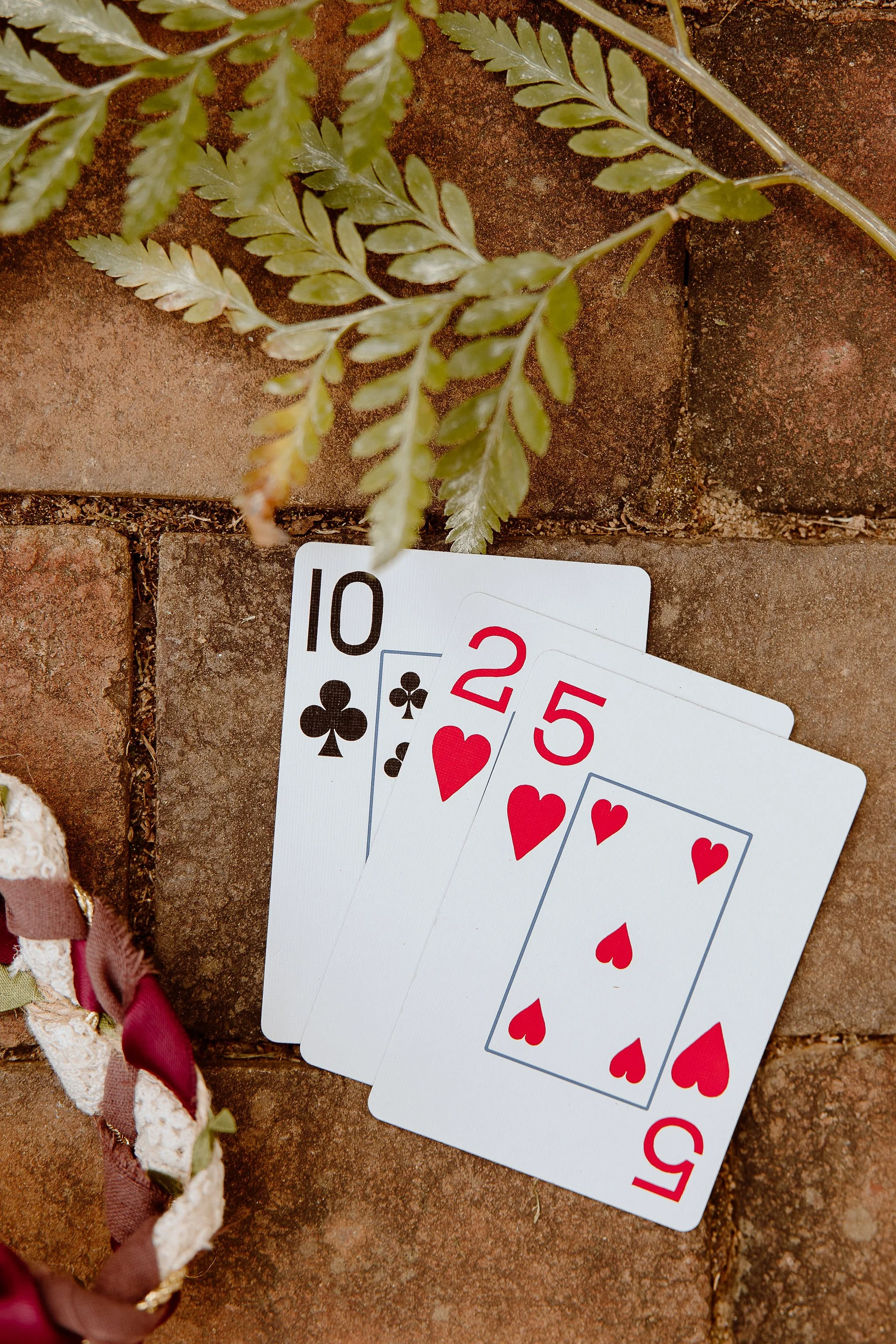 Display of three playing cards (10 of clubs, 2 of hearts, and 5 of hearts) representing the wedding date of October 25th for an event hosted at Historic Jasmine, a private wedding venue located in Greater Richmond, Virginia.