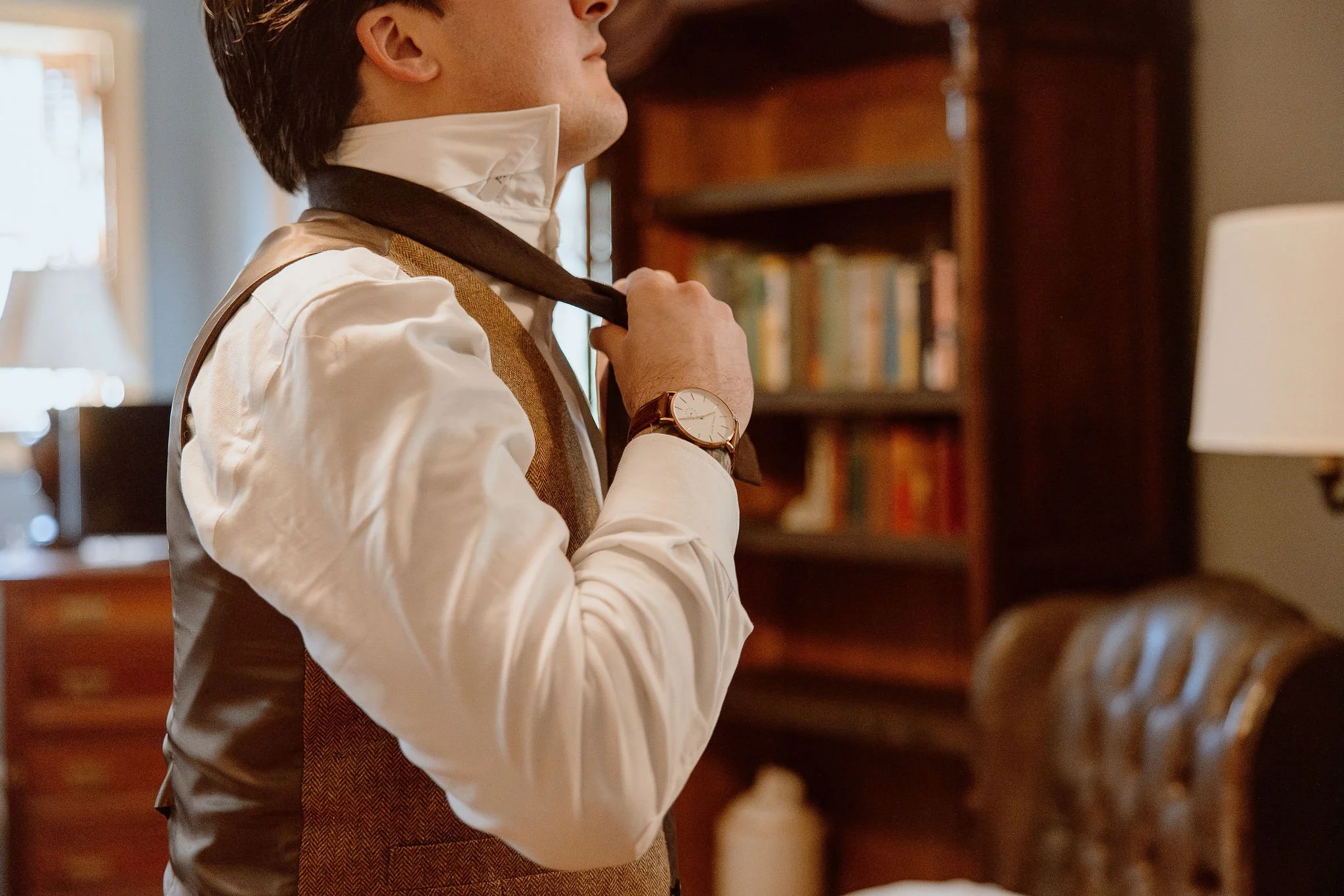 Groom puts on his tie before the wedding ceremony at Historic Jasmine, a private wedding venue in Greater Richmond, Virginia.