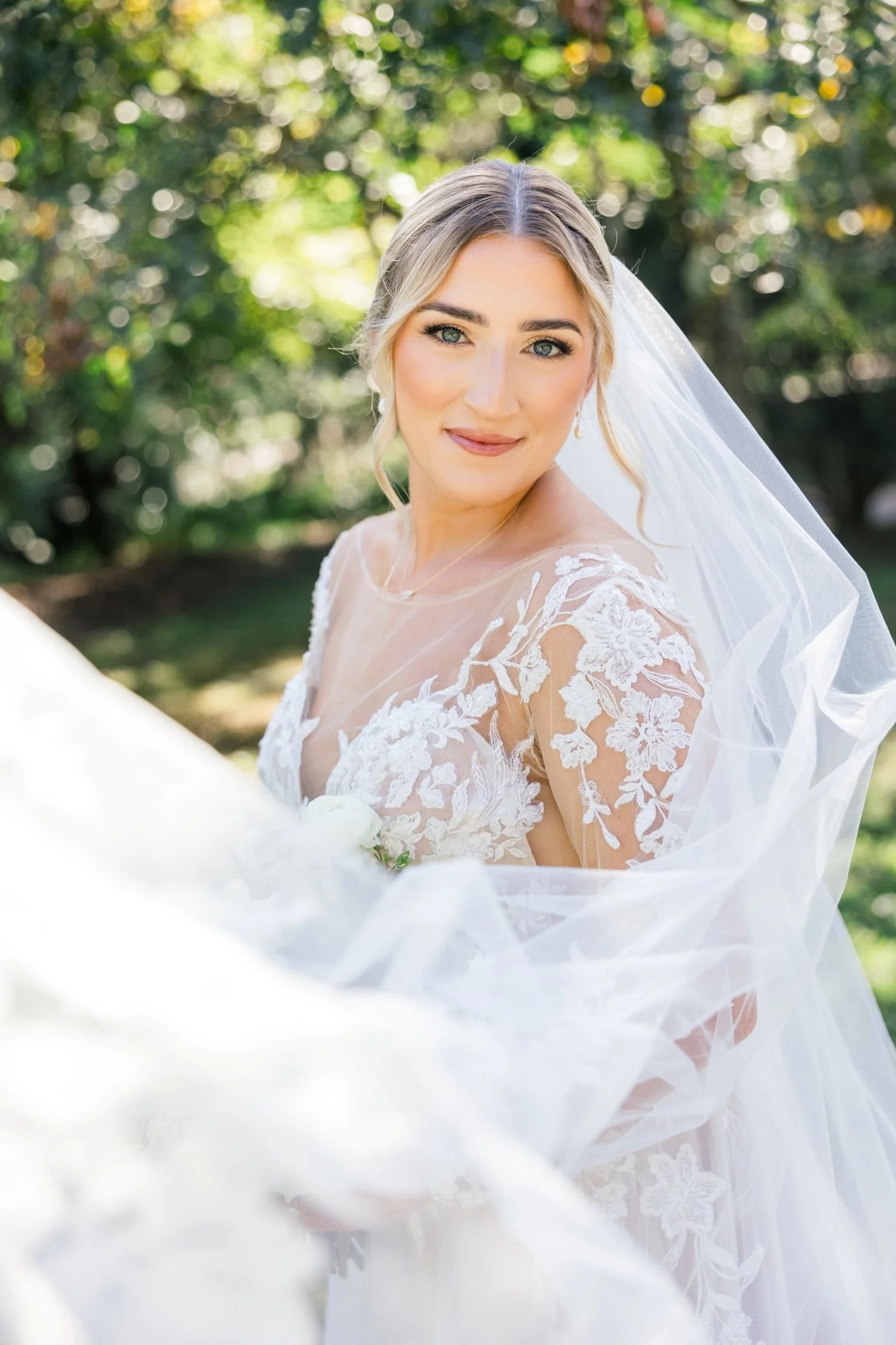 A bride poses with a long flowing veil in the secret garden of Historic Jasmine, a premiere wedding venue in Providence Forge, Virginia.  