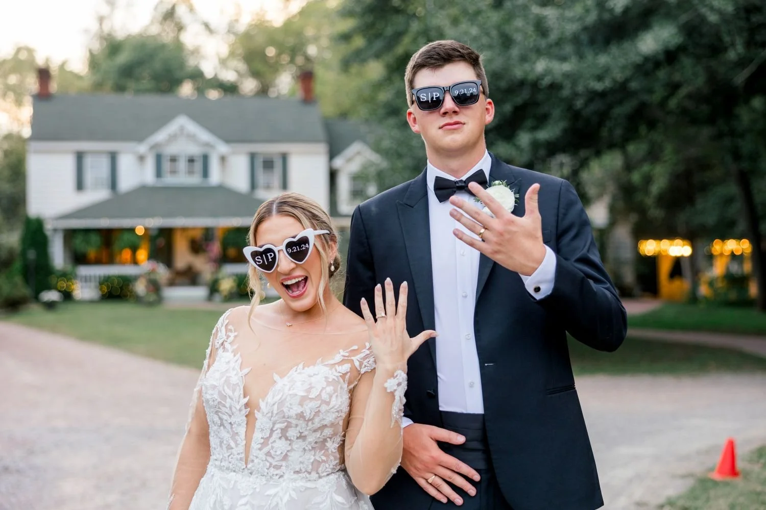 A bride and groom wearing sunglasses, showing off their new wedding rings in front of the Manor House at Historic Jasmine in New Kent, VA.