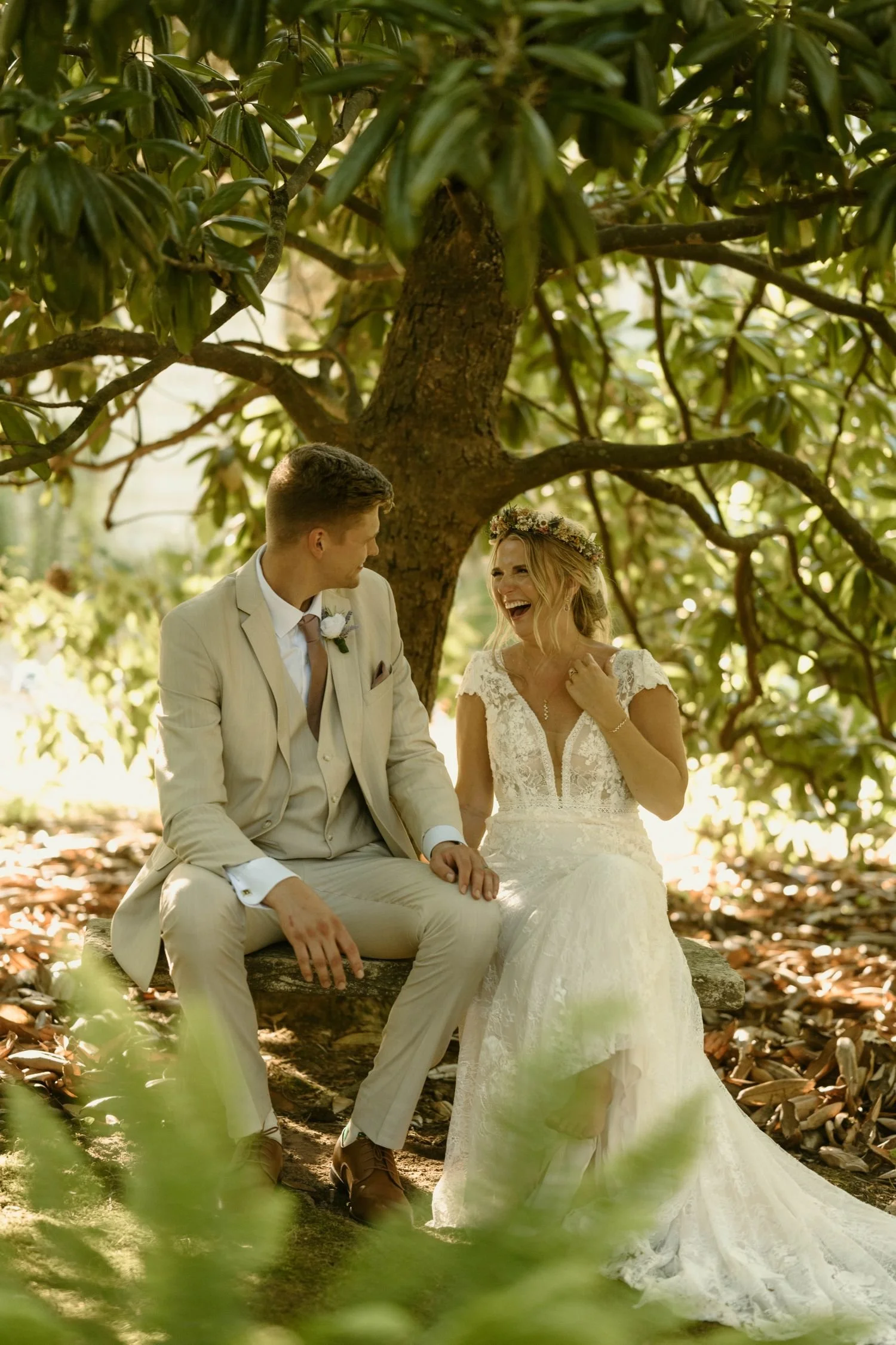A bride and groom smile and laugh beneath a magnolia tree at a secret garden wedding.  Historic Jasmine a private wedding venue near Richmond, Virginia.