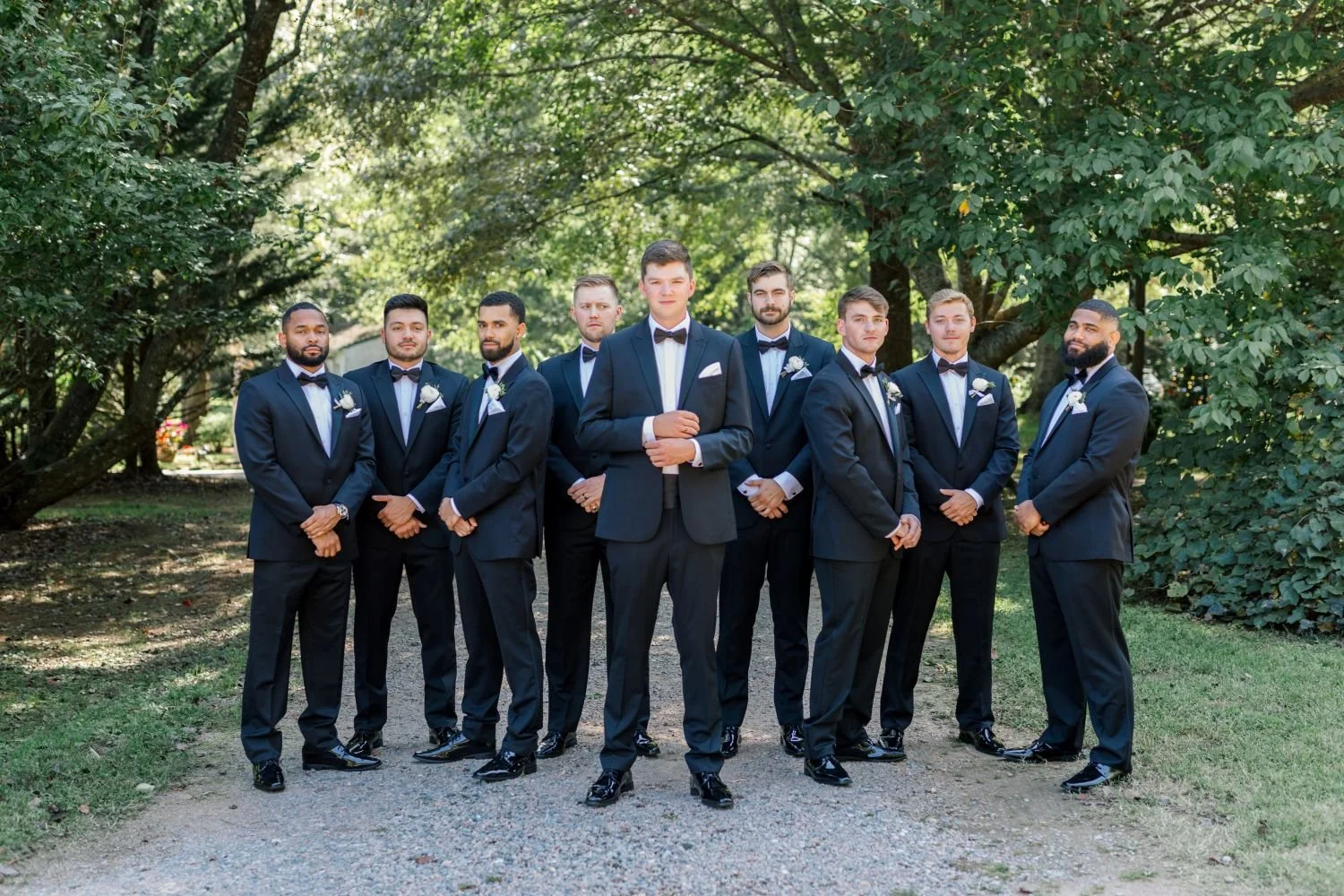 A groom and groomsmen pose for a portrait in a wooded grove at Historic Jasmine, a romantic garden wedding venue near Richmond, Virginia