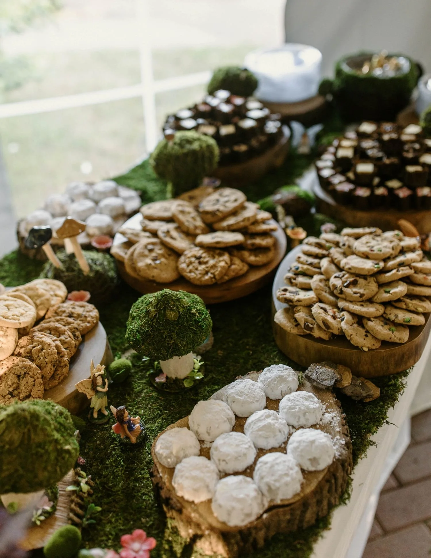 An enchanting fairytale dessert display featuring assorted cookies among moss covered mushrooms and miniature fairies.