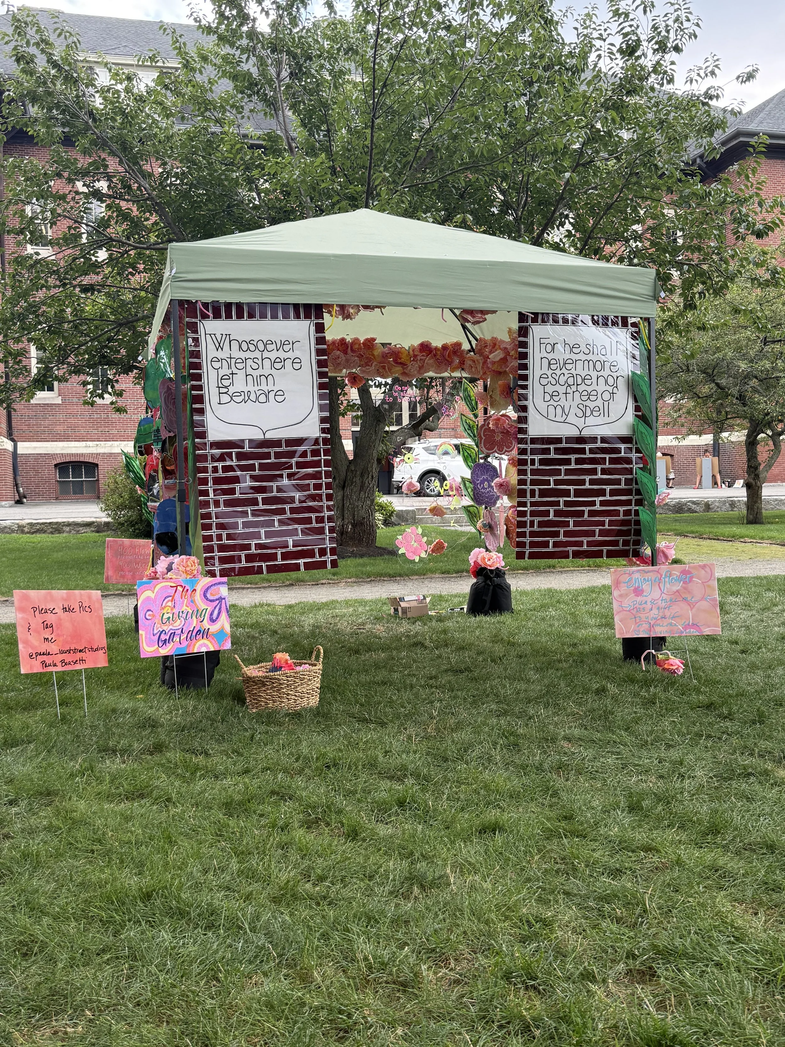 Outdoor installation display with multiple handwritten signs and colorful painted panels beneath a green canopy.