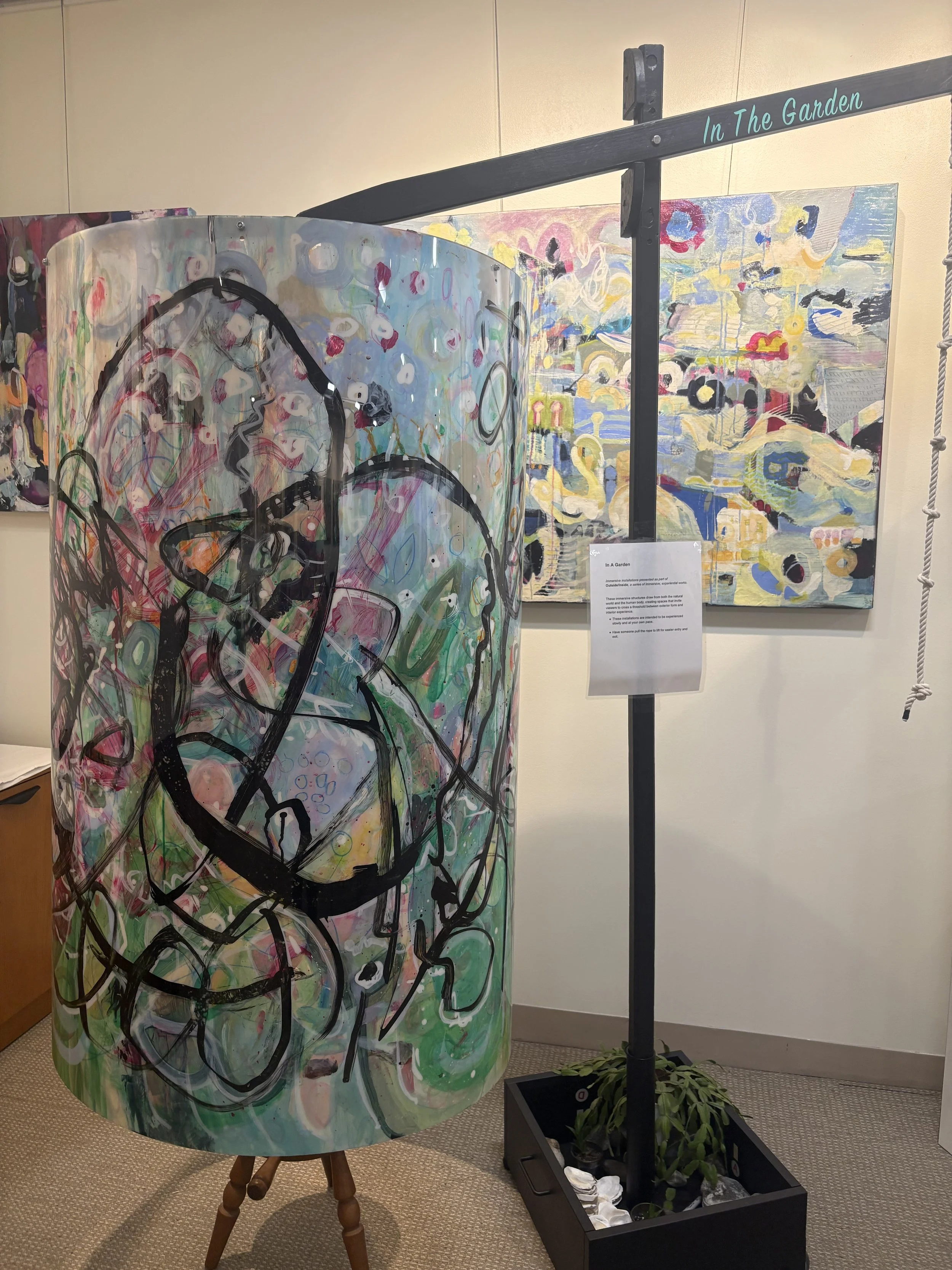 Curved translucent painted panel with black linework and pastel colors displayed indoors on a stand.
