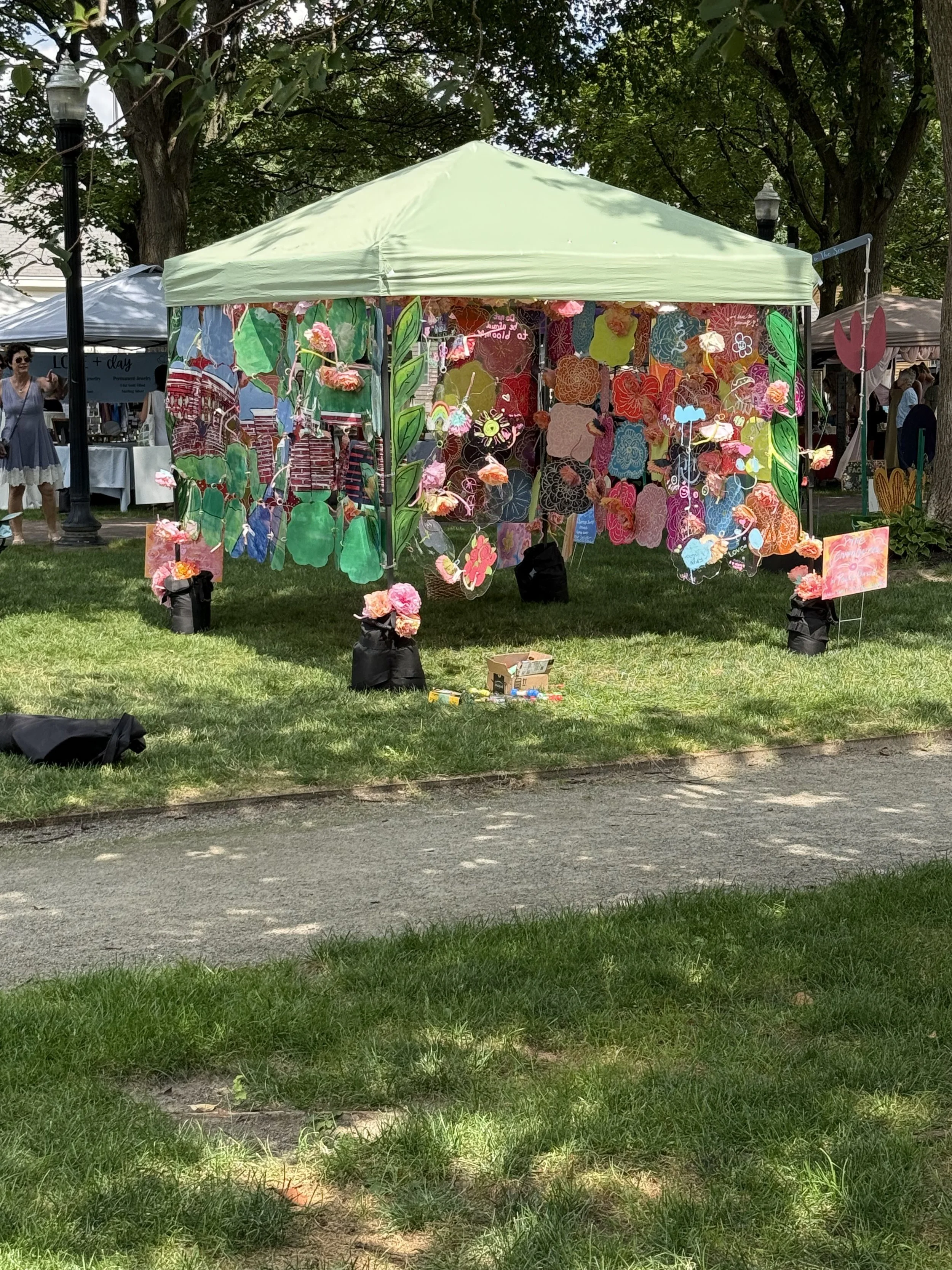 Side view of a green canopy transformed with painted translucent panels and hanging pink flowers.