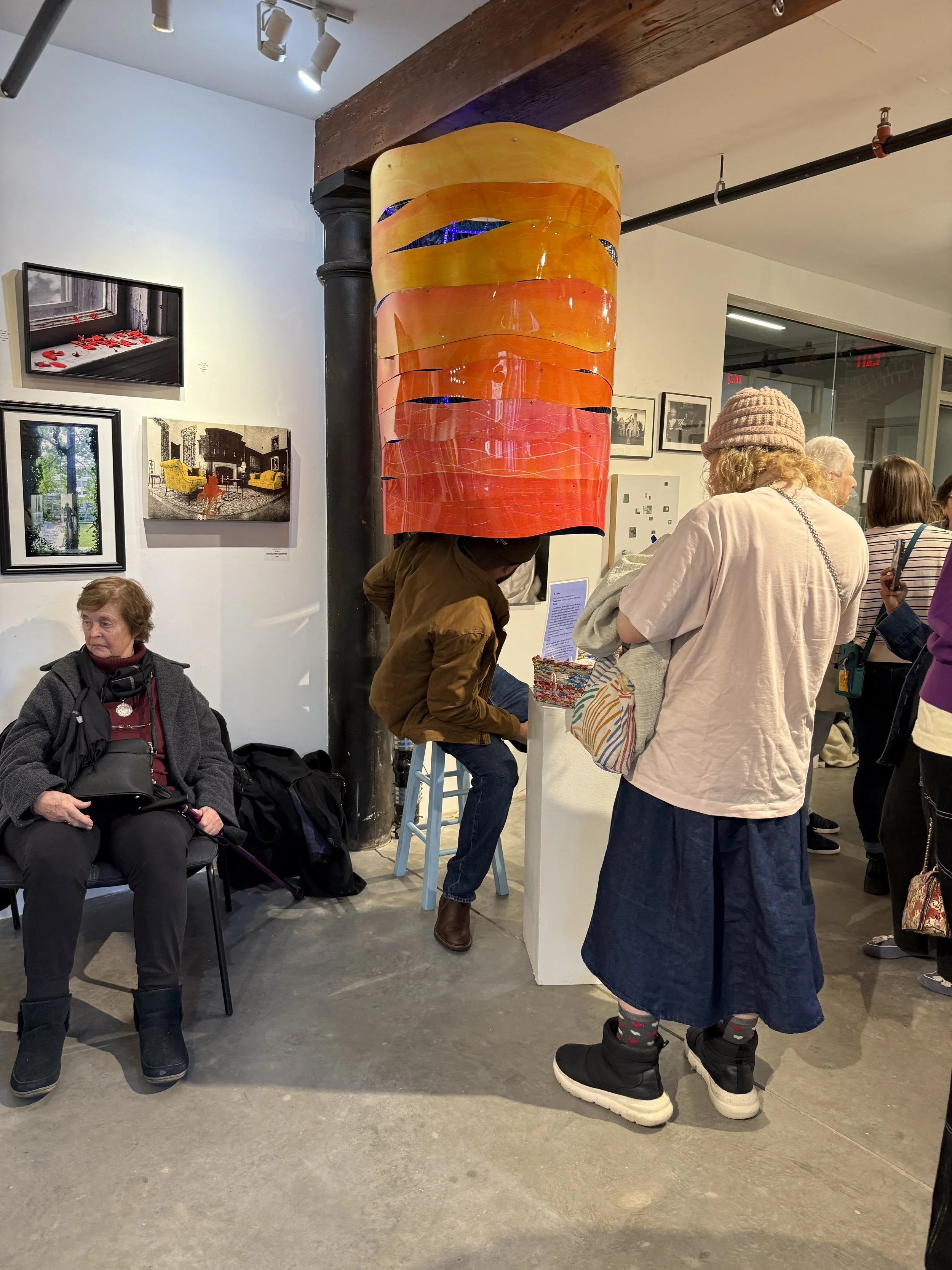 Gallery visitors viewing a glowing orange-and-pink cylindrical sculpture and accompanying artworks.
