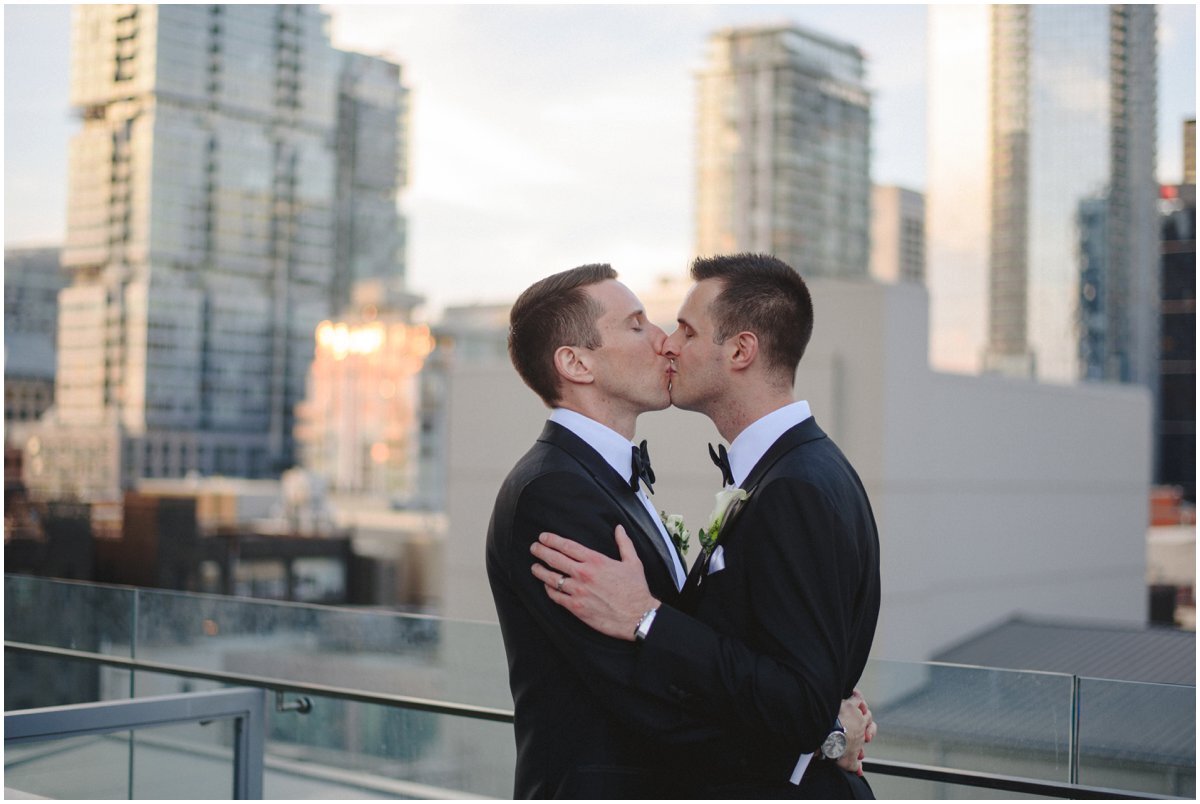 Same sex couple kissing at sunset with Toronto Skyline at Malaparte