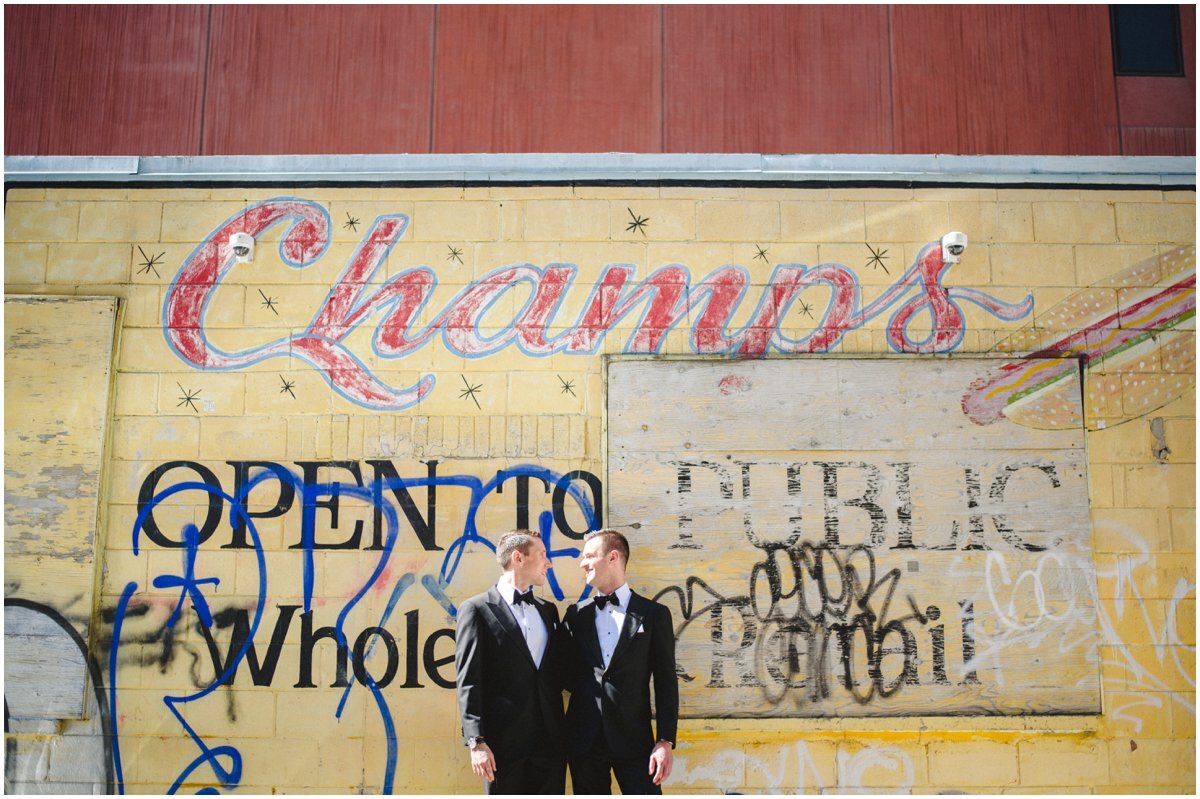 Two grooms in stylish suits with bow ties in downtown Toronto in front of a graffiti wall