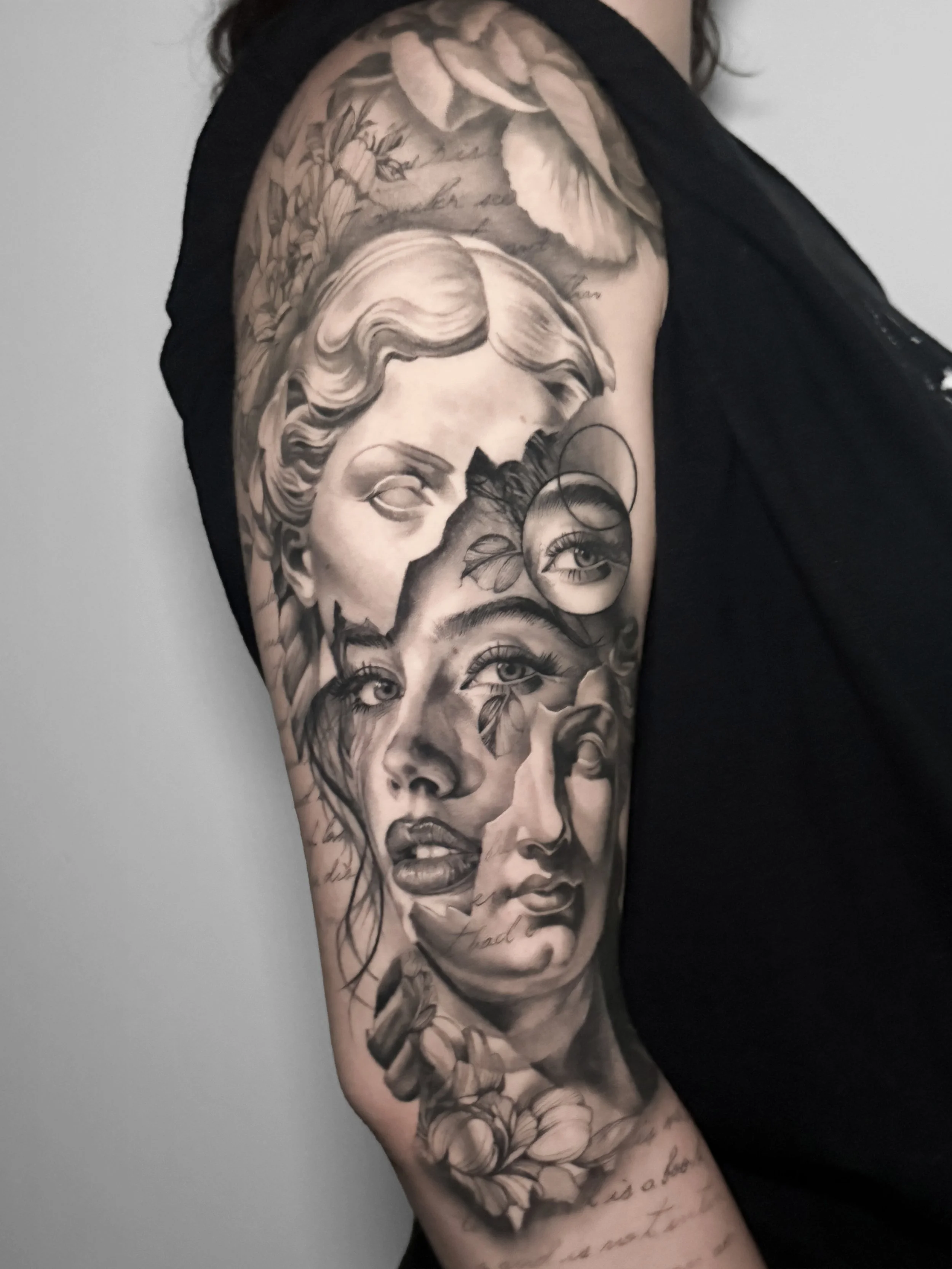 Realistic Black and gray tattoo on person's upper arm and shoulder depicting multiple faces, flowers, and handwritten script.