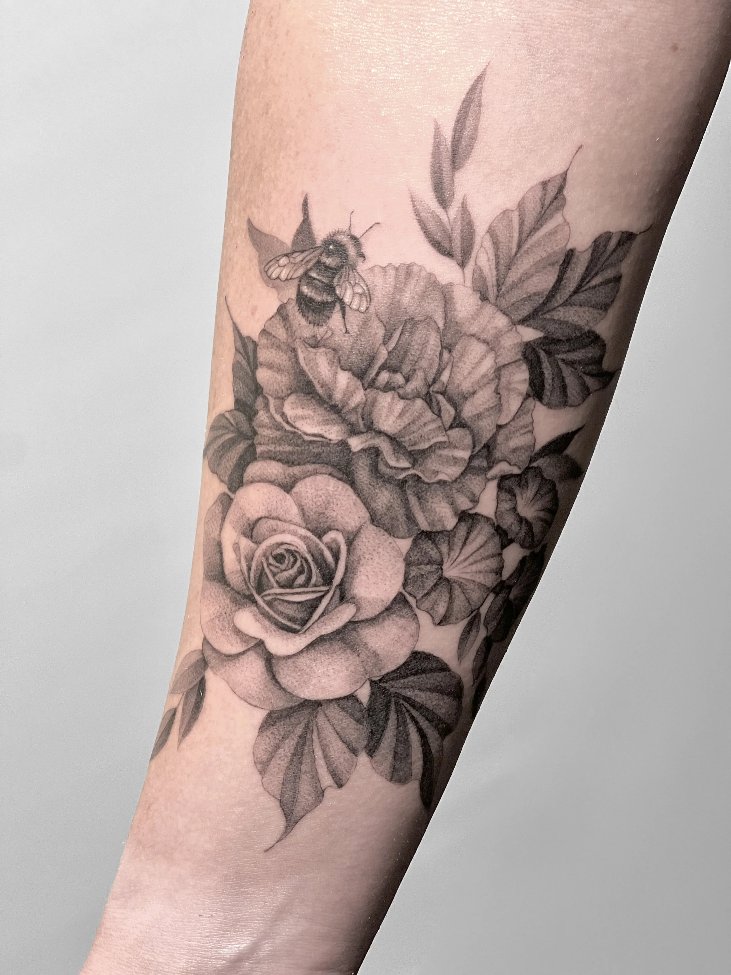 Black and gray tattoo of a bee on a flower with leaves.