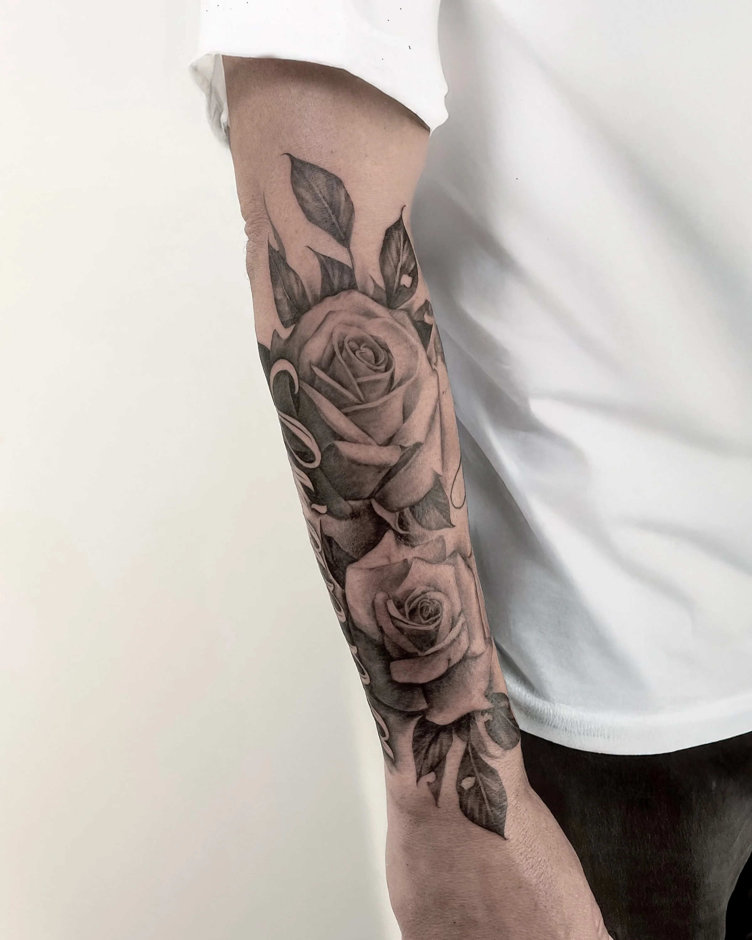 A person's arm with a detailed black and gray tattoo of three roses with leaves.