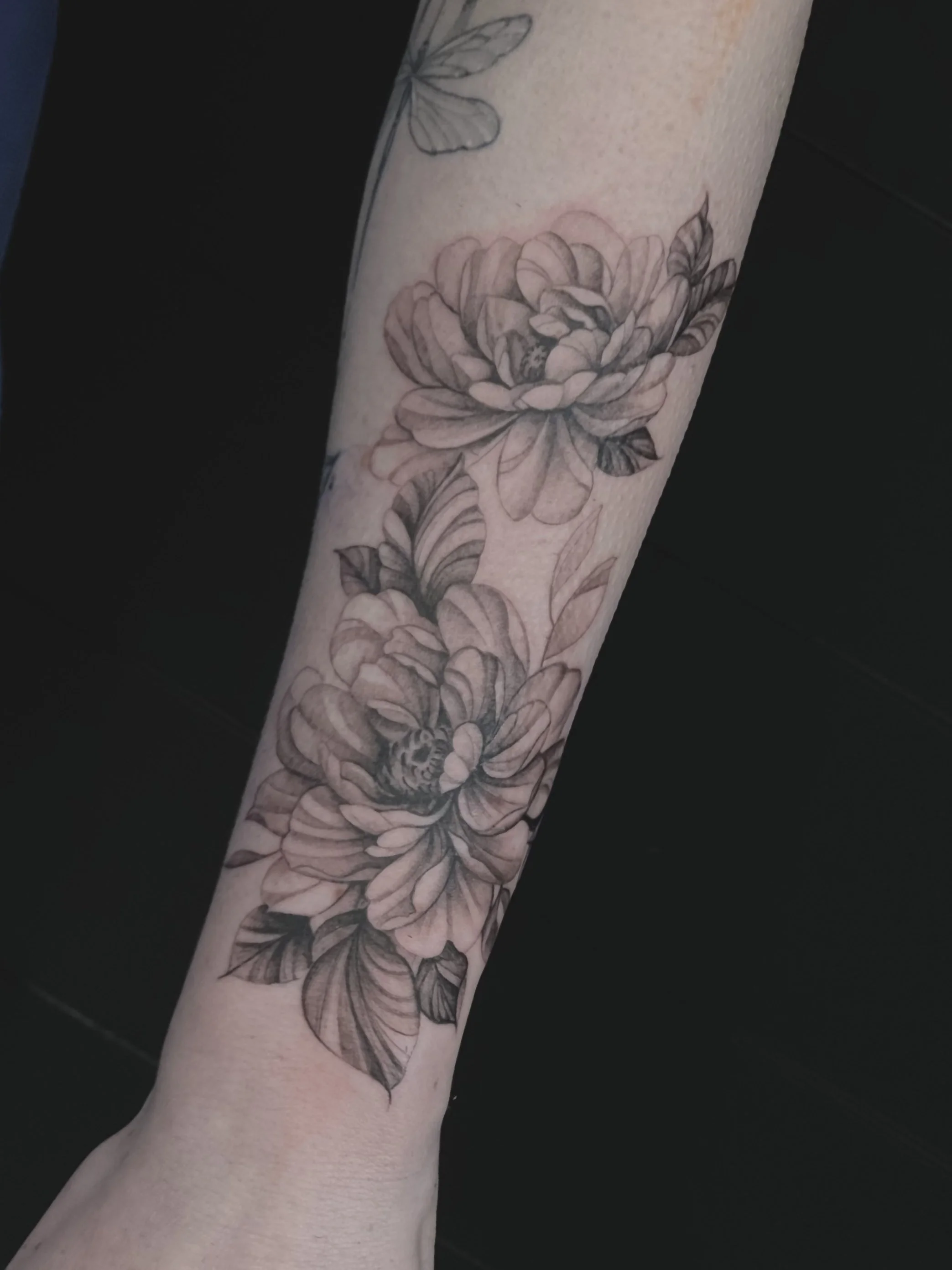 A tattoo of two large peonies, with detailed petals and leaves, and a butterfly on the top part of the arm.