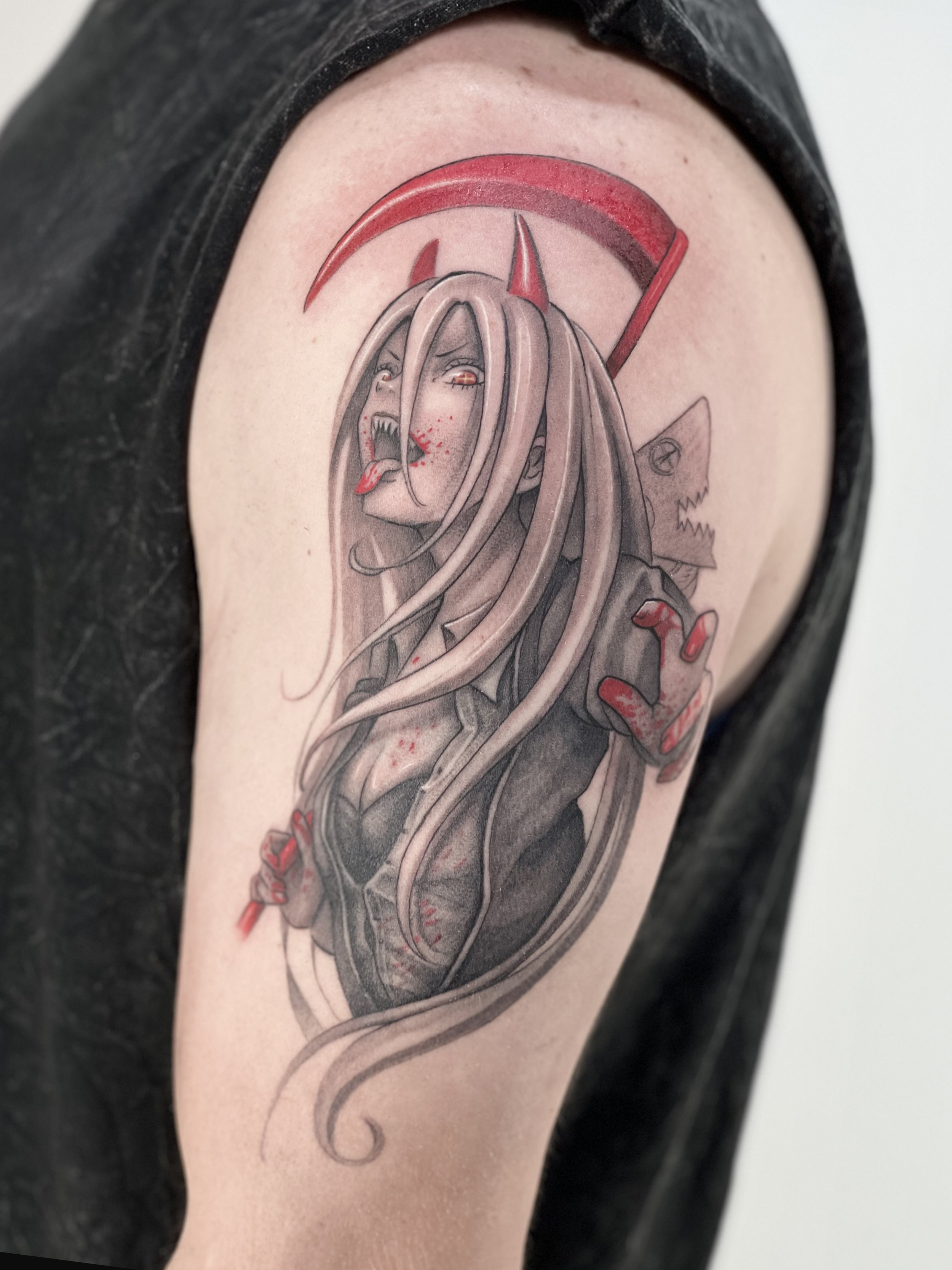 A tattoo of a demon-like woman with long hair, horns, and a tongue sticking out. She has a fierce expression and blood splatters on her face and clothing, with a red sickle-shaped halo above her head and a wolf head in the background.