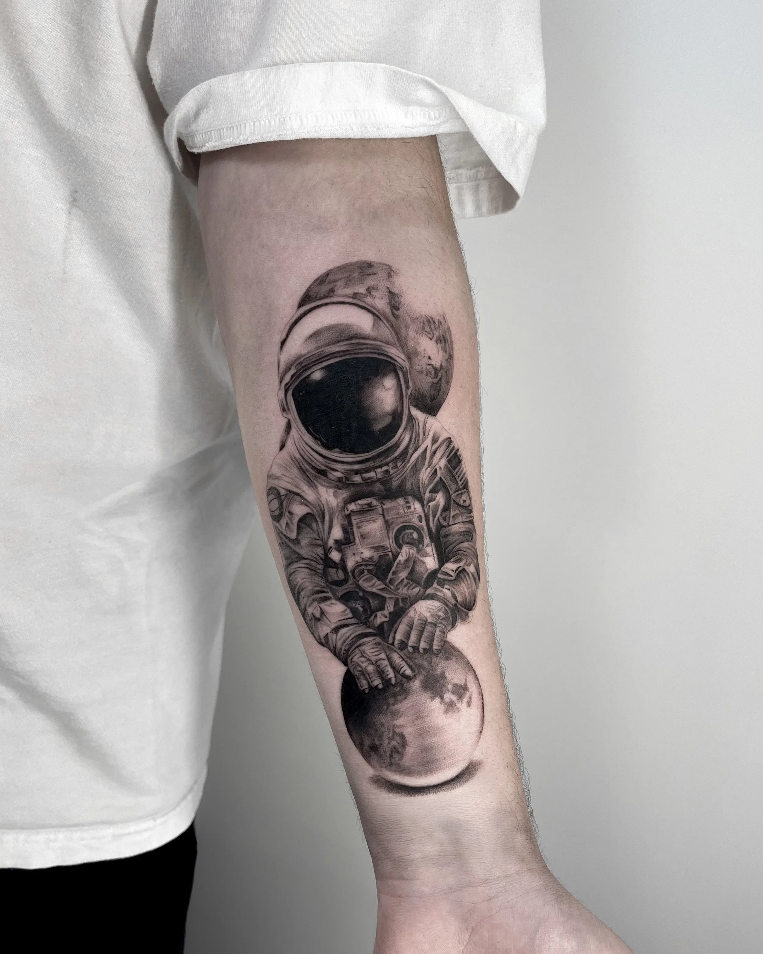 Tattoo of an astronaut floating in space, with planets in the background and holding the moon.