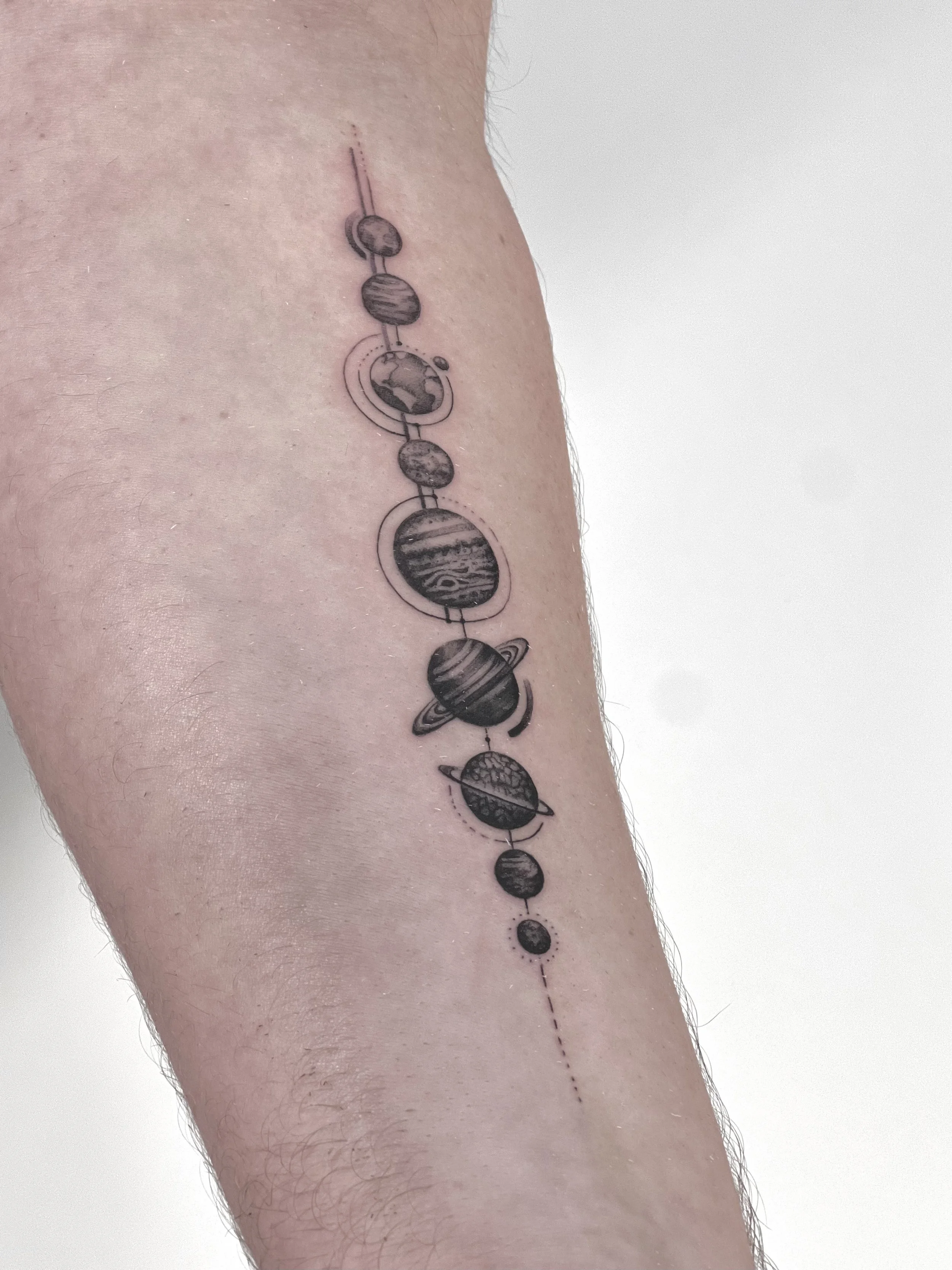 Black and gray tattoo of planets within a line on a person's arm, representing the solar system.