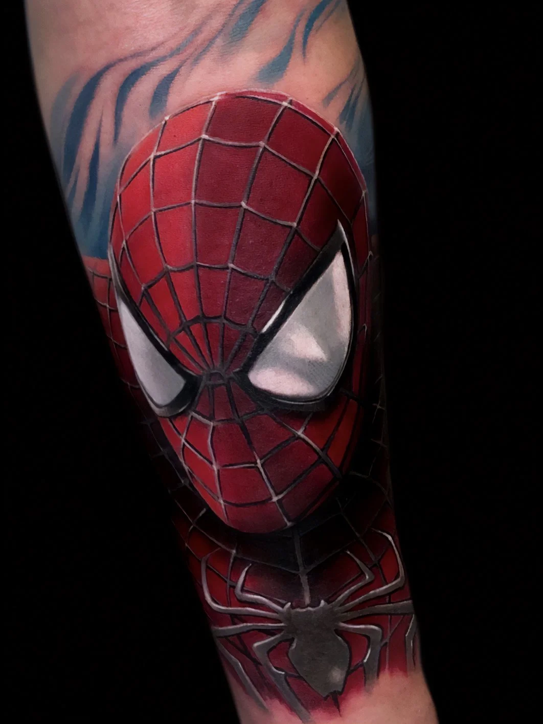 Close-up of one of the best Spider-Man tattoos with red and black webbed mask and black eyes, with a black spider symbol below.