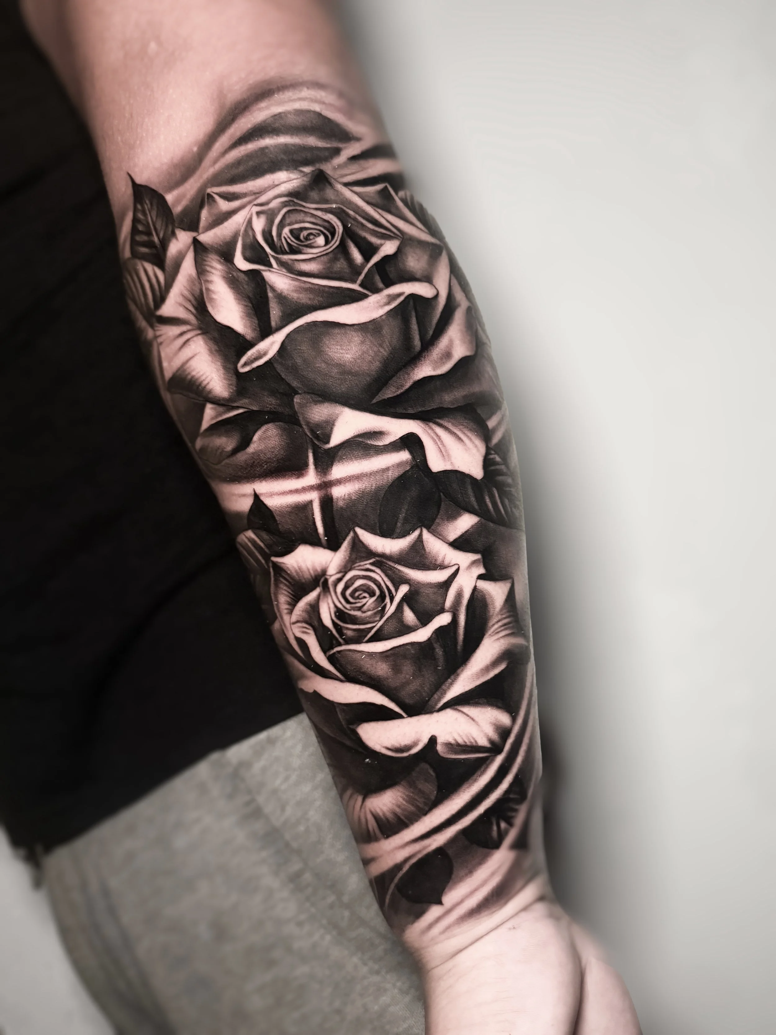 A black and gray realistic tattoo of two roses on a person's forearm.