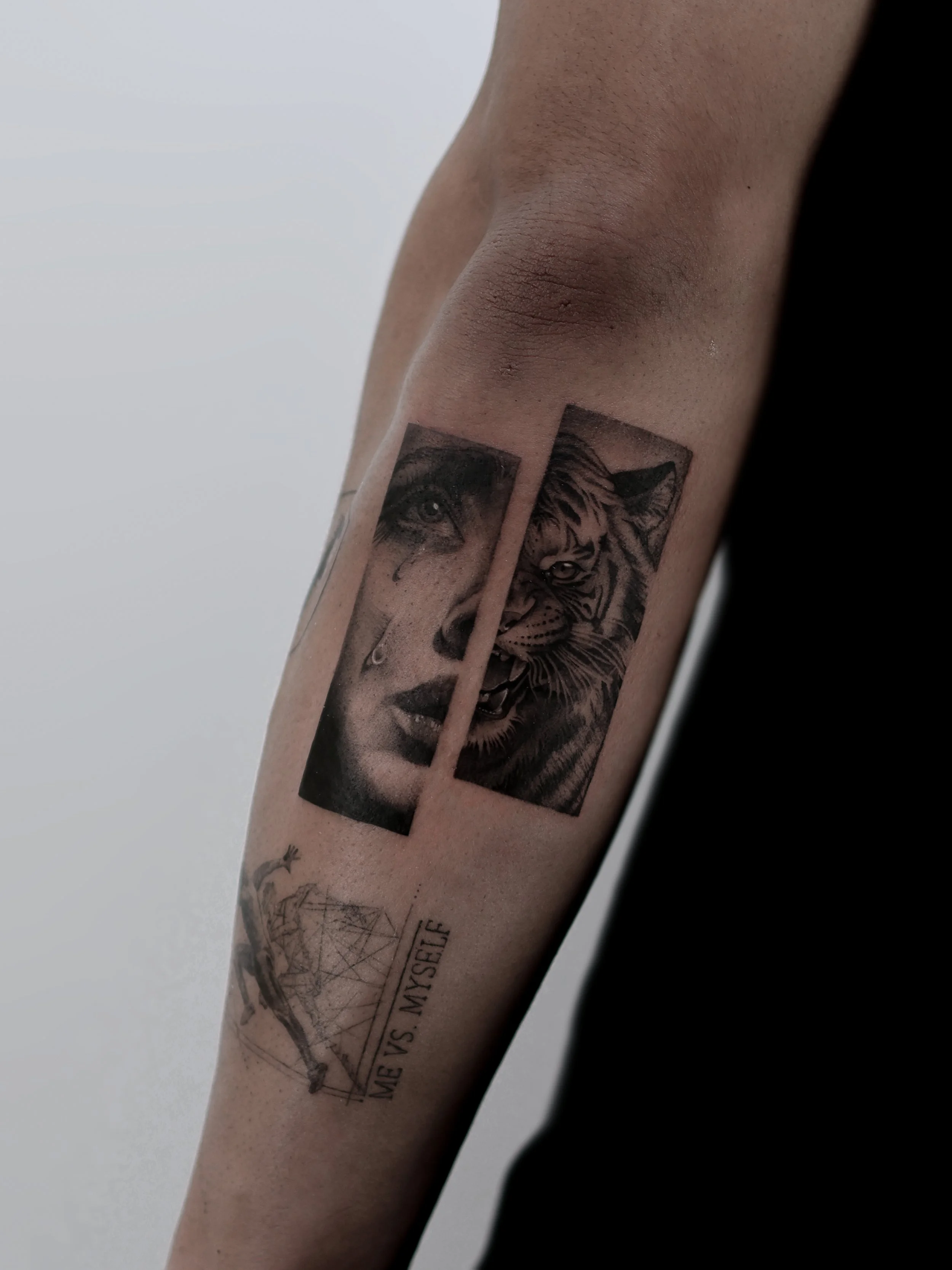 Tattoo of a woman's face with tears and a tiger's face in black and gray ink on a person's forearm, with a geometric design and the phrase "ME VS. MYSELF" below.