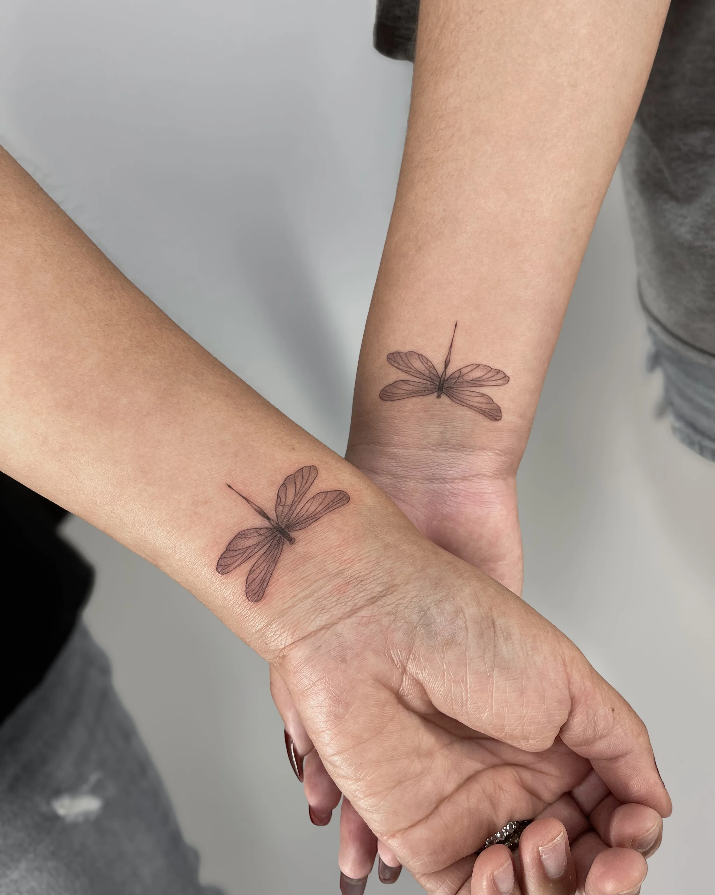 Two people with matching butterfly tattoos holding hands.