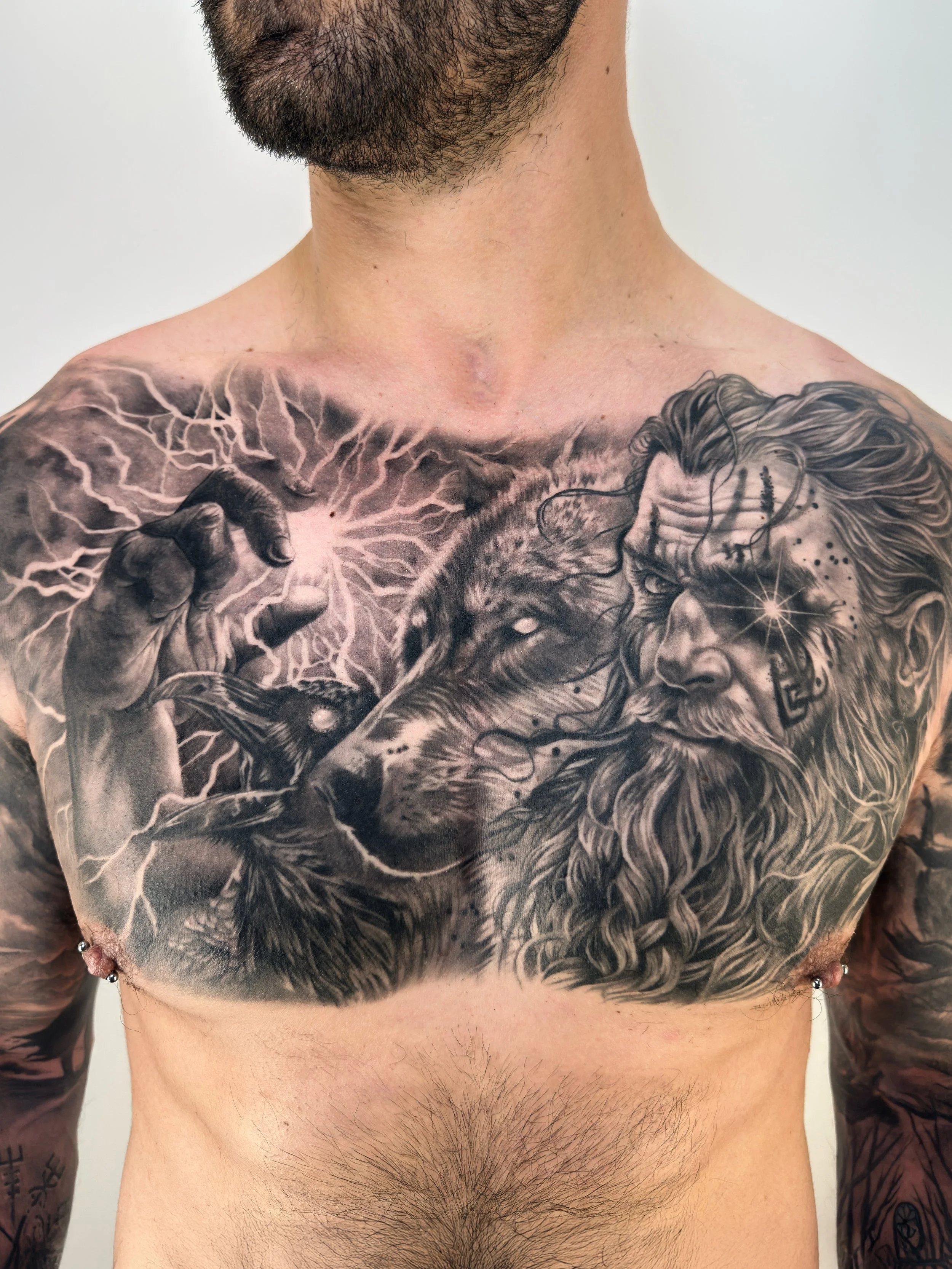 Close-up of a man's chest tattoo depicting a wizard with a long beard, a wolf, a hand holding a glowing orb with lightning in the background, and a woman with a star on her forehead.
