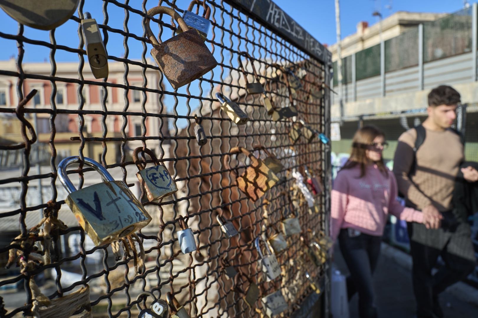 Lucchetti dell’amore su una recinzione mentre una coppia cammina mano nella mano.
Matteo Della Torre Photography
Fotografo di ritratto, beauty, moda e commerciale. Ritratti e Book per modelle e modelli. 
Studio: San Ferdinando di Puglia (BT).