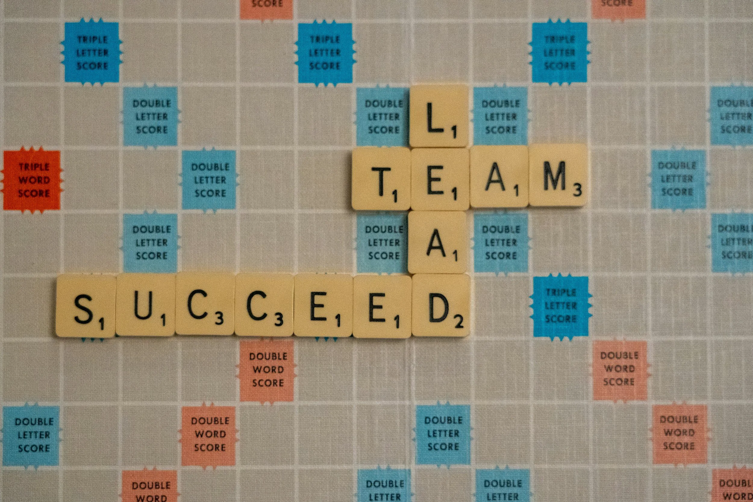 scrabble board with letter tiles that read Lead, Team, Succeed