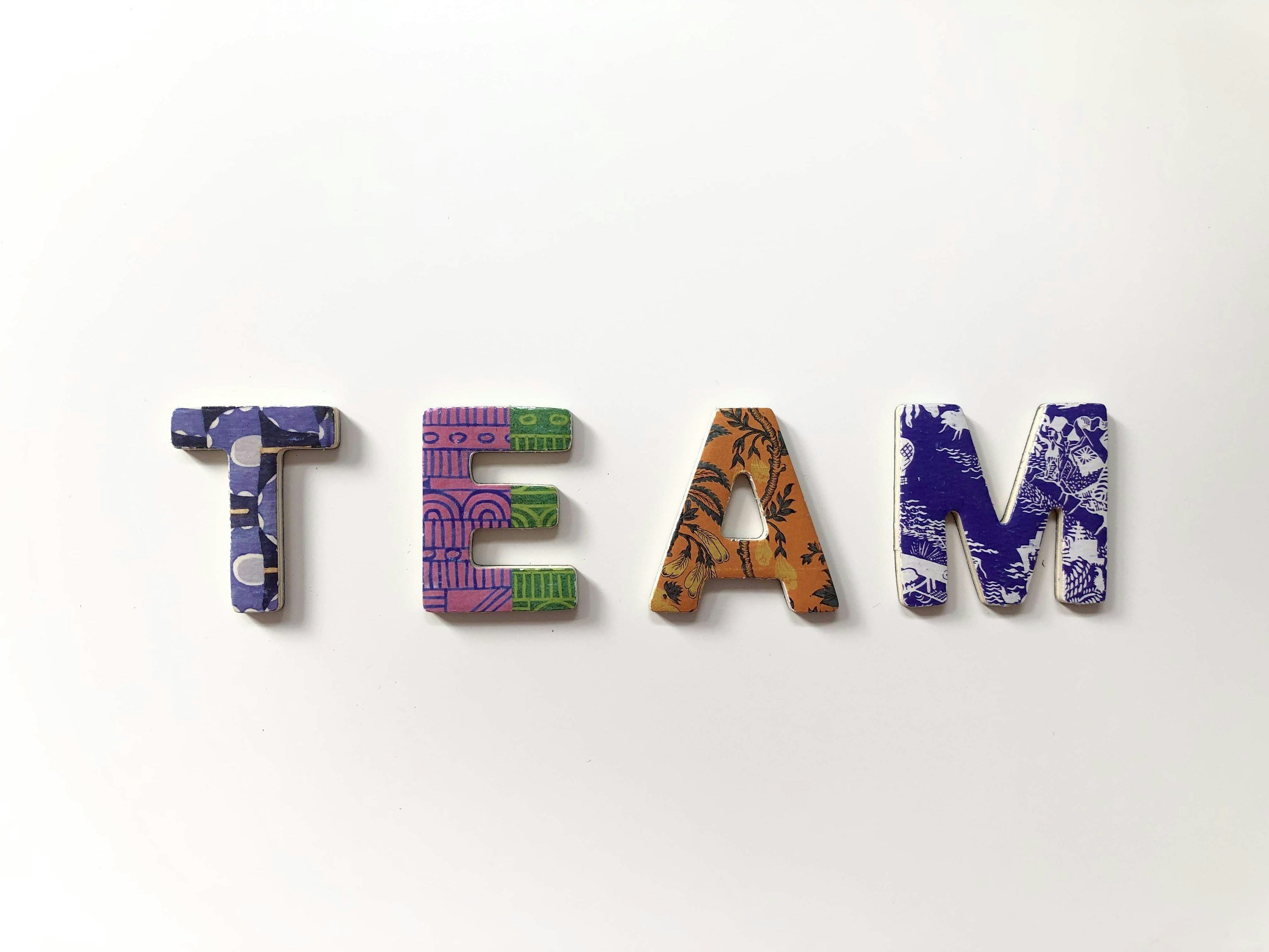 4 cardboard cut-out letters on a white background, spelling out "TEAM", each letter with a unique colourful pattern design on it