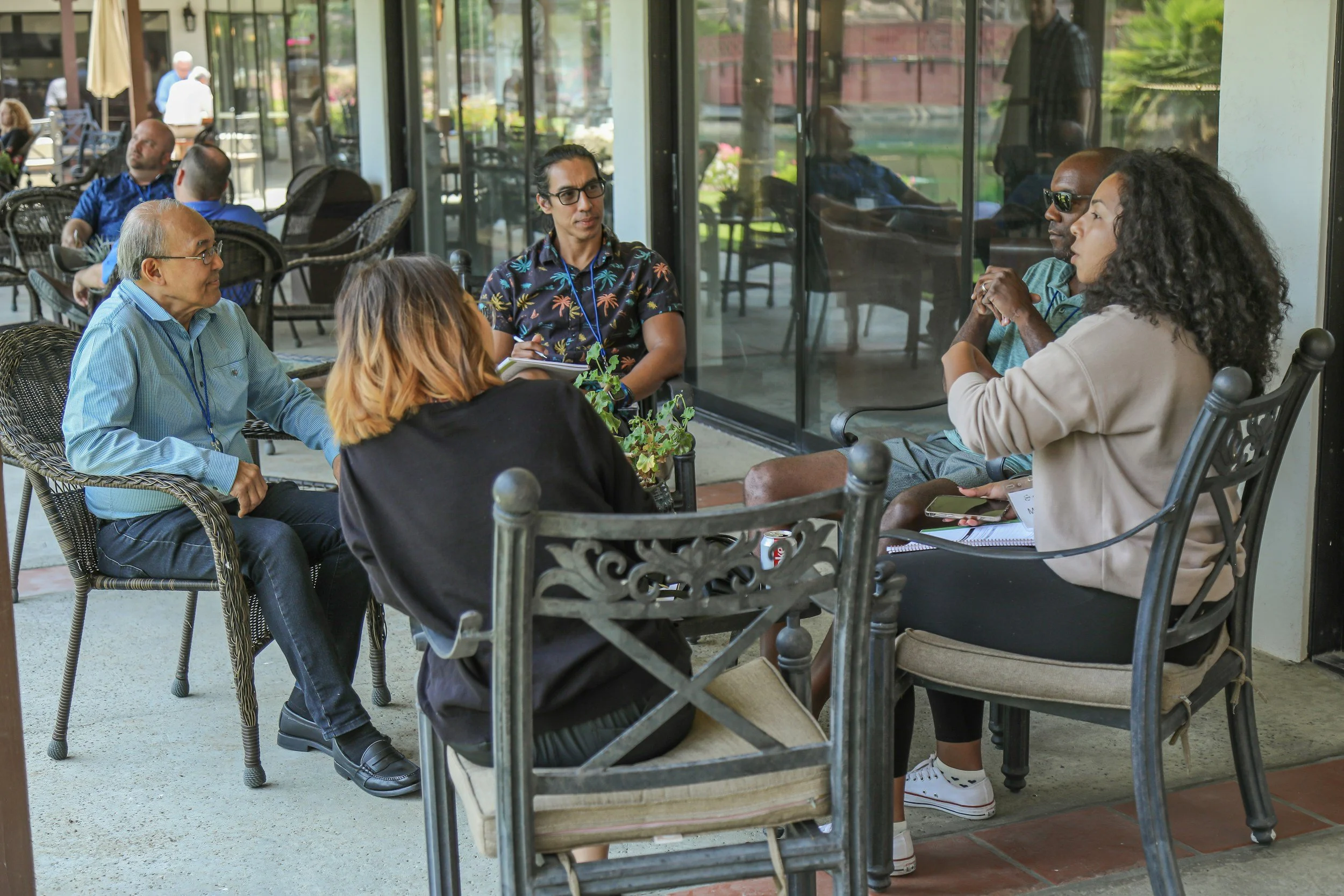 A group of 5 people from diverse racial backgrounds, genders and age groups meeting in a circle at an outdoor patio