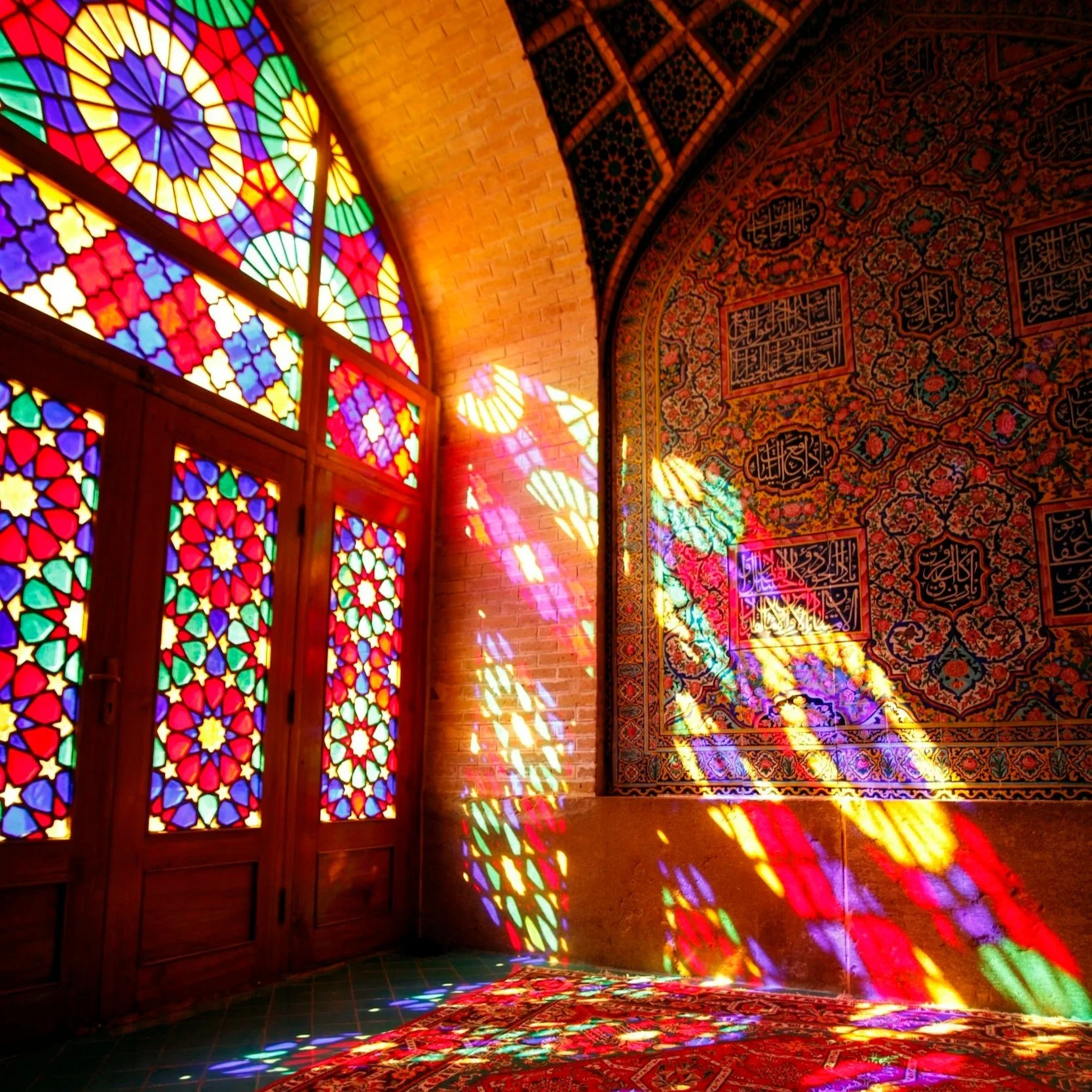 Sun streaming through colourful geometric stain glass windows into an Iranian architectural space with Persian rugs on the ground
