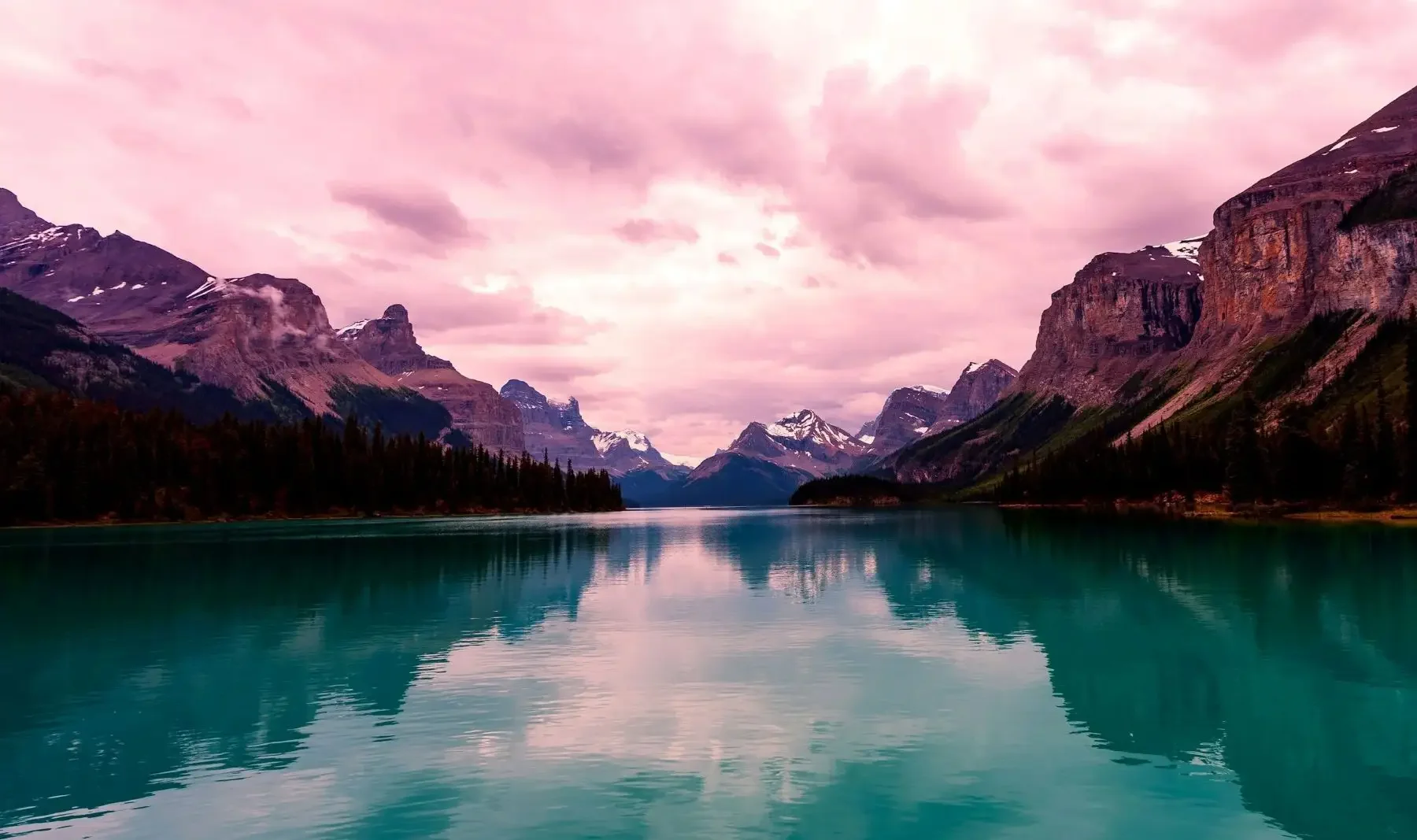 A view of a pink sky above mountains from a blue lake.