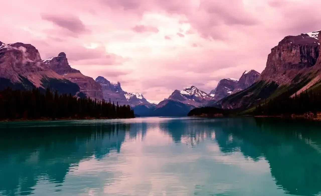 Pink sky above mountains with bright blue water  at the base.