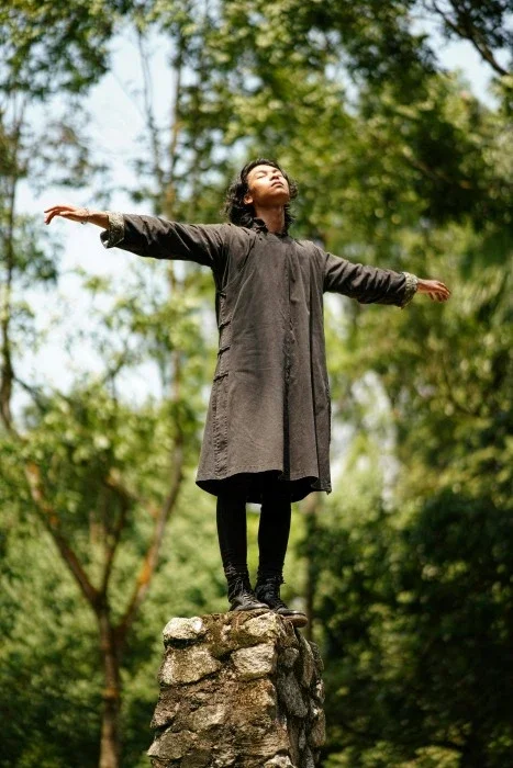 A person standing with their arms wide open in the woods.