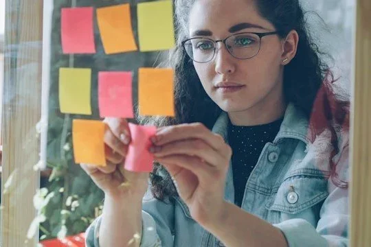 A woman carefully placing post-it-notes on a mirror.