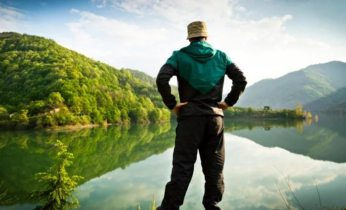 A man standing in front of a lake at the foot of a mountain.