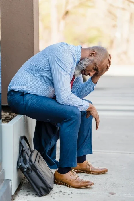A man sitting outside, leaning down on his legs and looking sad.