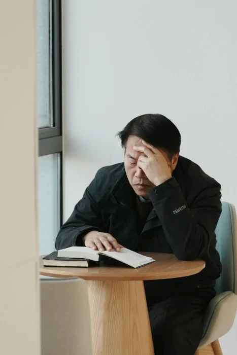 A man with his head in his hand and eyes closed, reading a book.